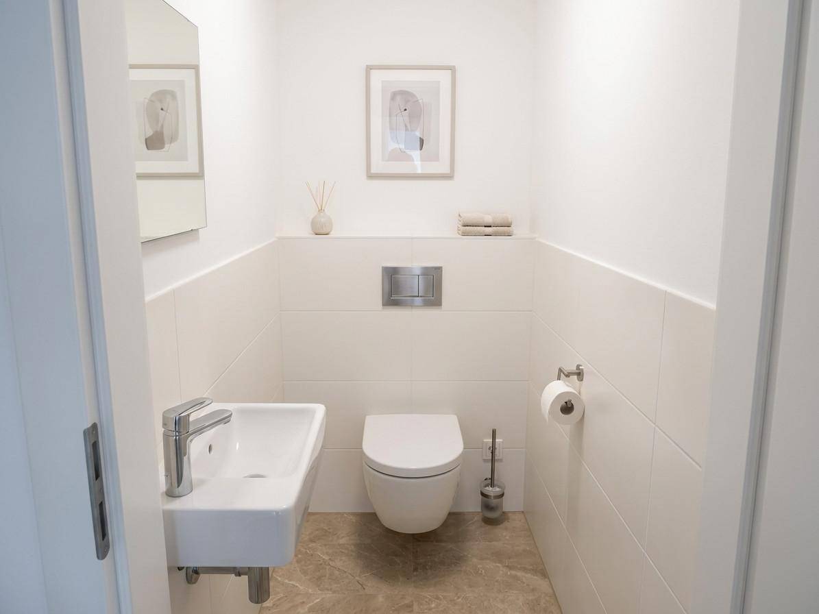 Modernes Gäste-WC mit wandhängender Toilette, kleinem Waschbecken und Fliesenboden.