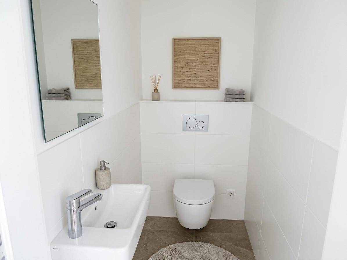 Modernes Gäste-WC mit wandhängender Toilette, Waschbecken und Spiegel.