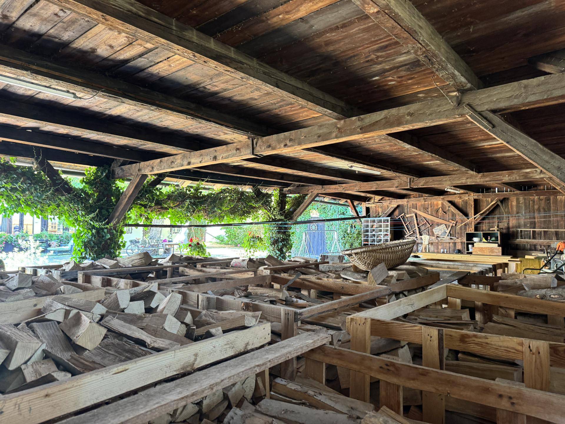 Innenansicht einer Scheune mit Holzbalkenkonstruktion und gestapeltem Brennholz.