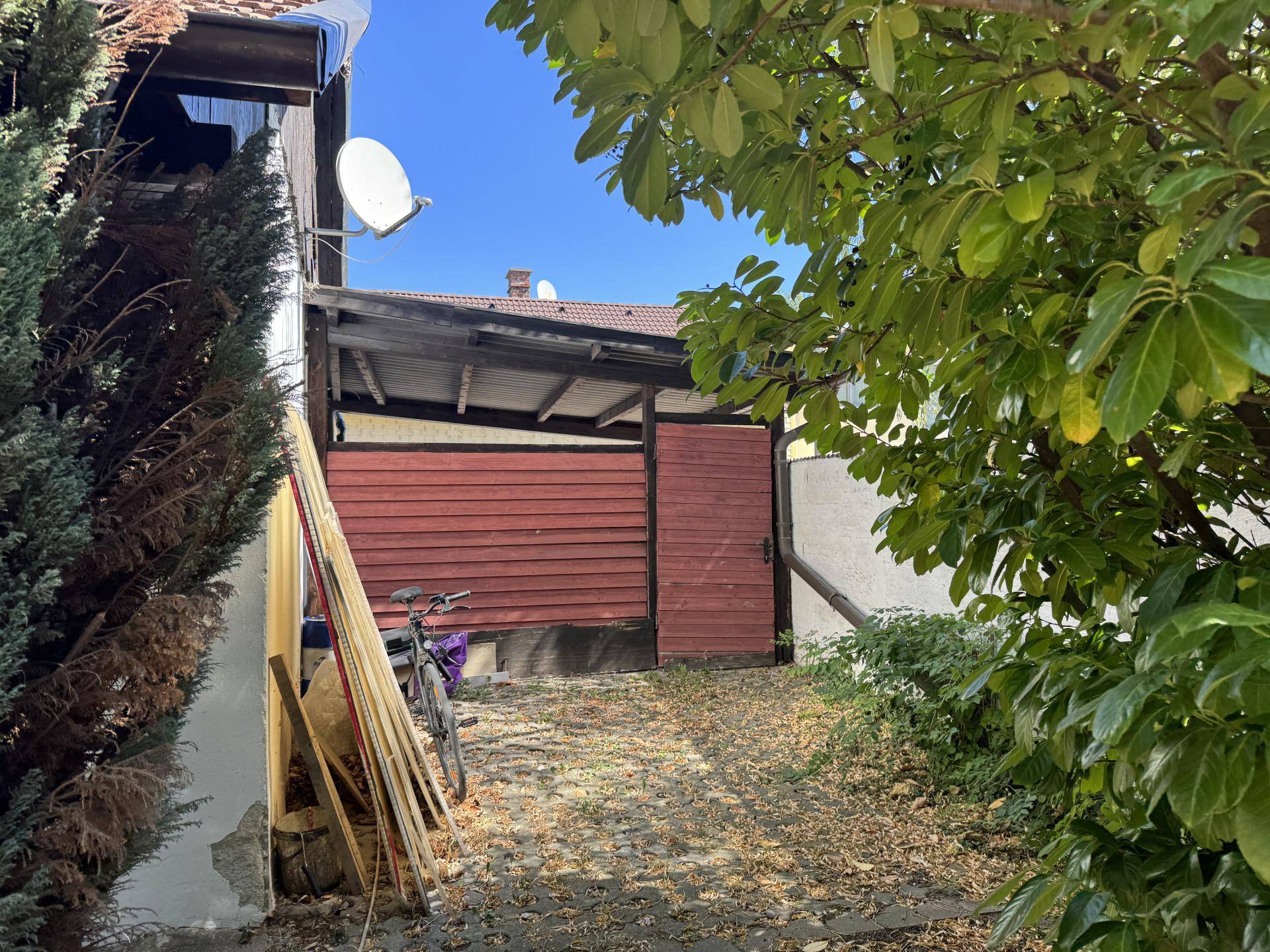 Schmaler Weg neben dem Haus mit überdachtem Bereich und Holzverkleidung.