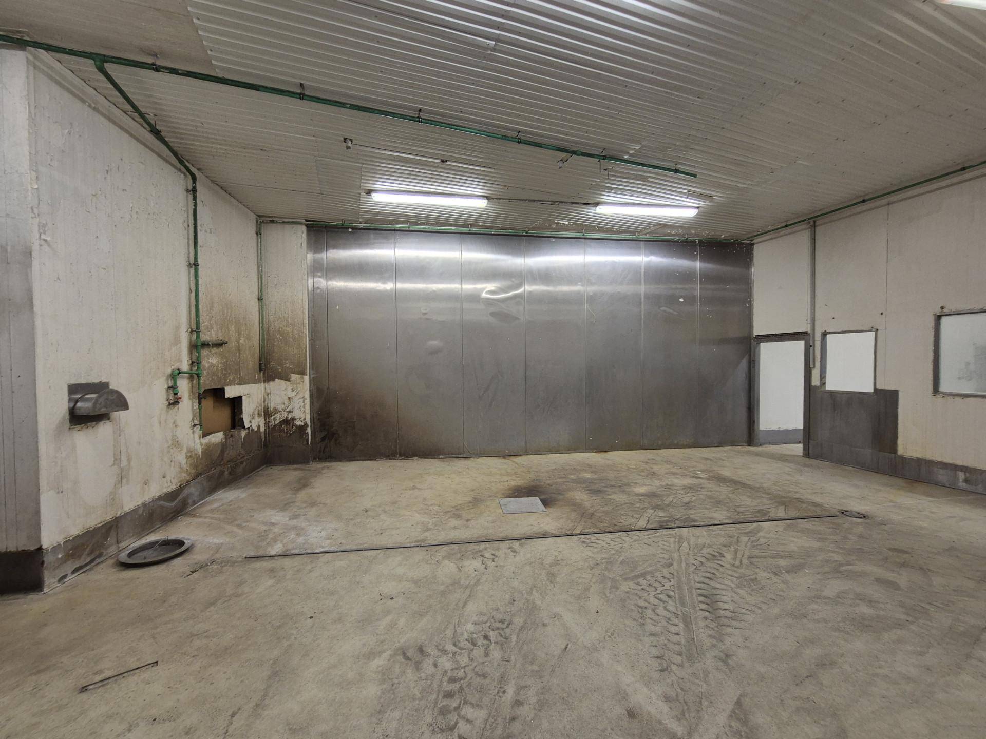 Industrieller Raum mit Metallverkleidung an der Wand, Betonboden und sichtbaren Leitungen.