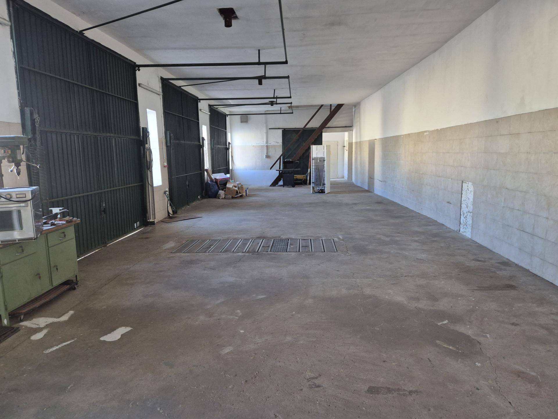 Großer, leerer Innenraum mit Betonboden und hohen Metalltoren, ideal als Lager oder Werkstatt.
