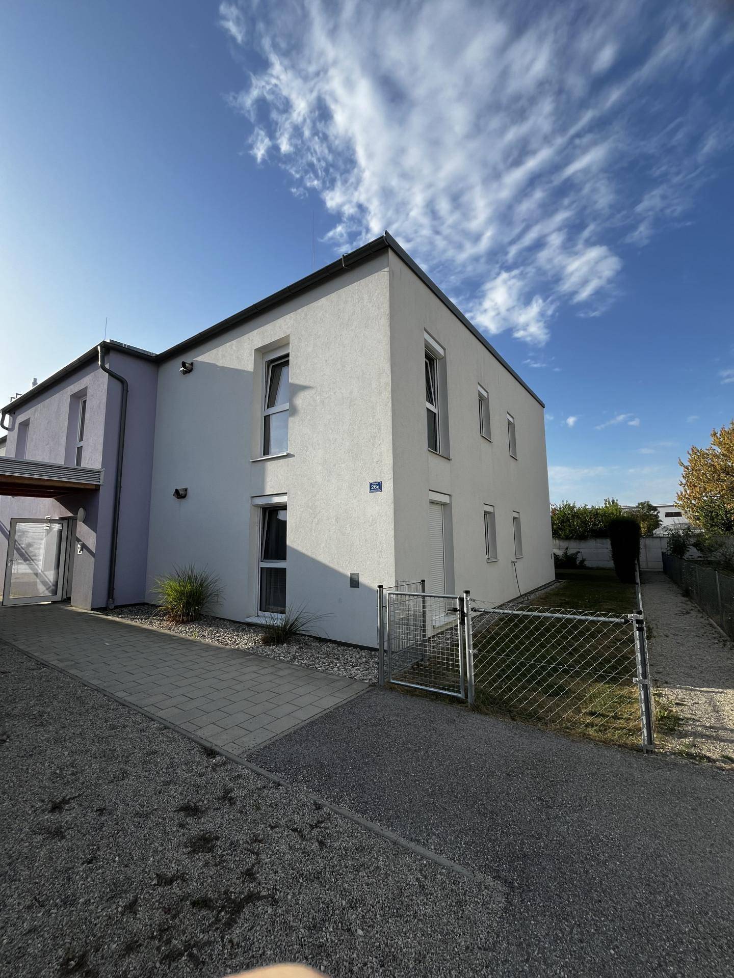 Modernes Wohngebäude mit weißer Fassade und gepflegtem Vorgarten unter blauem Himmel.