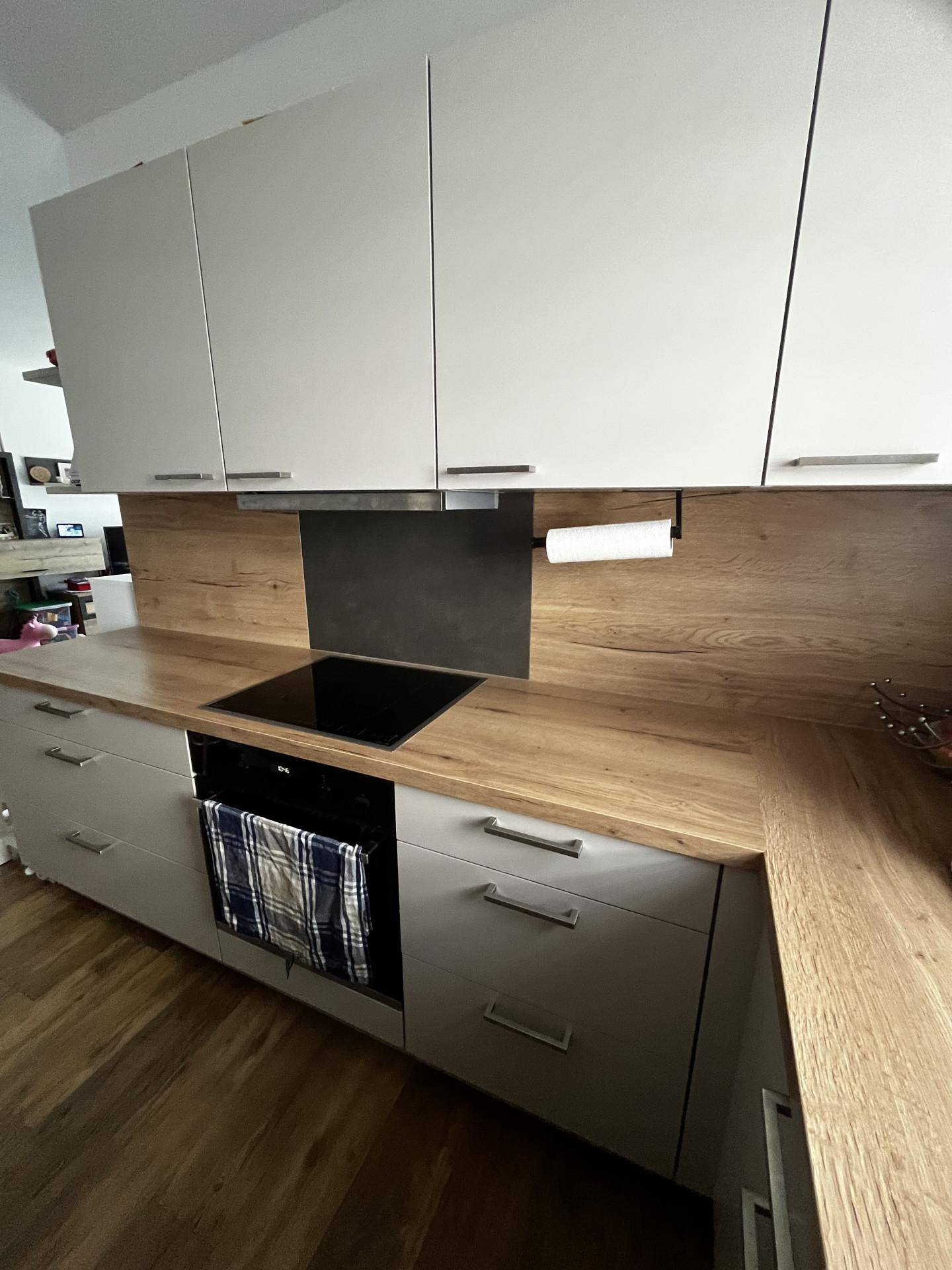 Detailansicht der modernen Küche mit Induktionskochfeld, Backofen und Holzdekor-Arbeitsplatte.