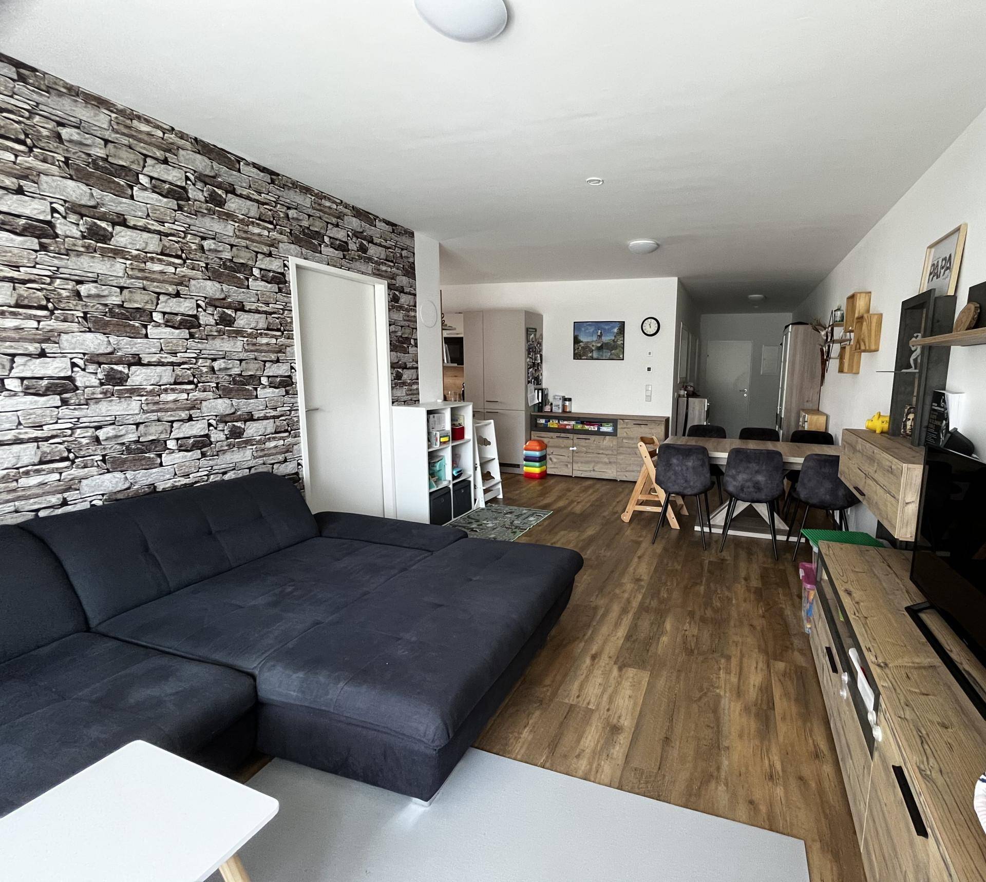 Offener Wohn- und Essbereich mit L-förmigem Sofa, Esstisch und Steinwand-Akzent.