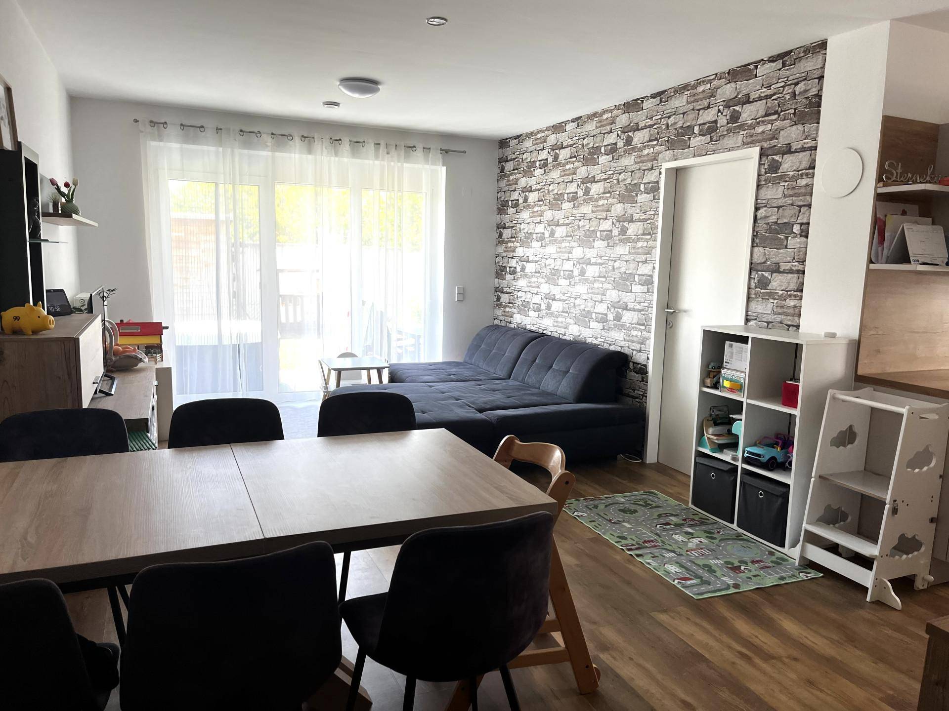 Wohnbereich mit Steinwand-Akzent, Sofa und Zugang zur Terrasse durch große Fenster.