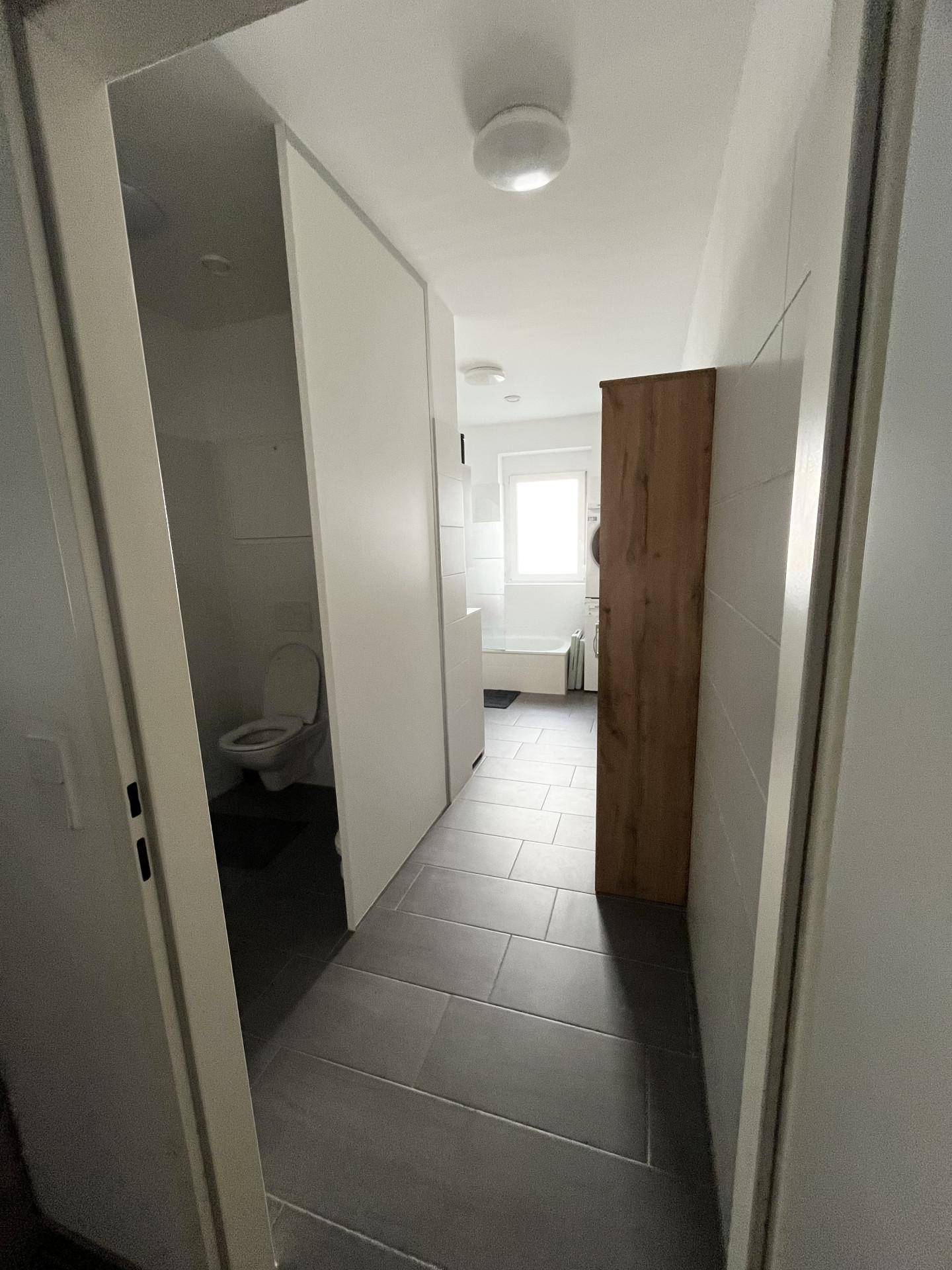 Heller Flur mit Fliesenboden, der zum Badezimmer und zur separaten Toilette führt.