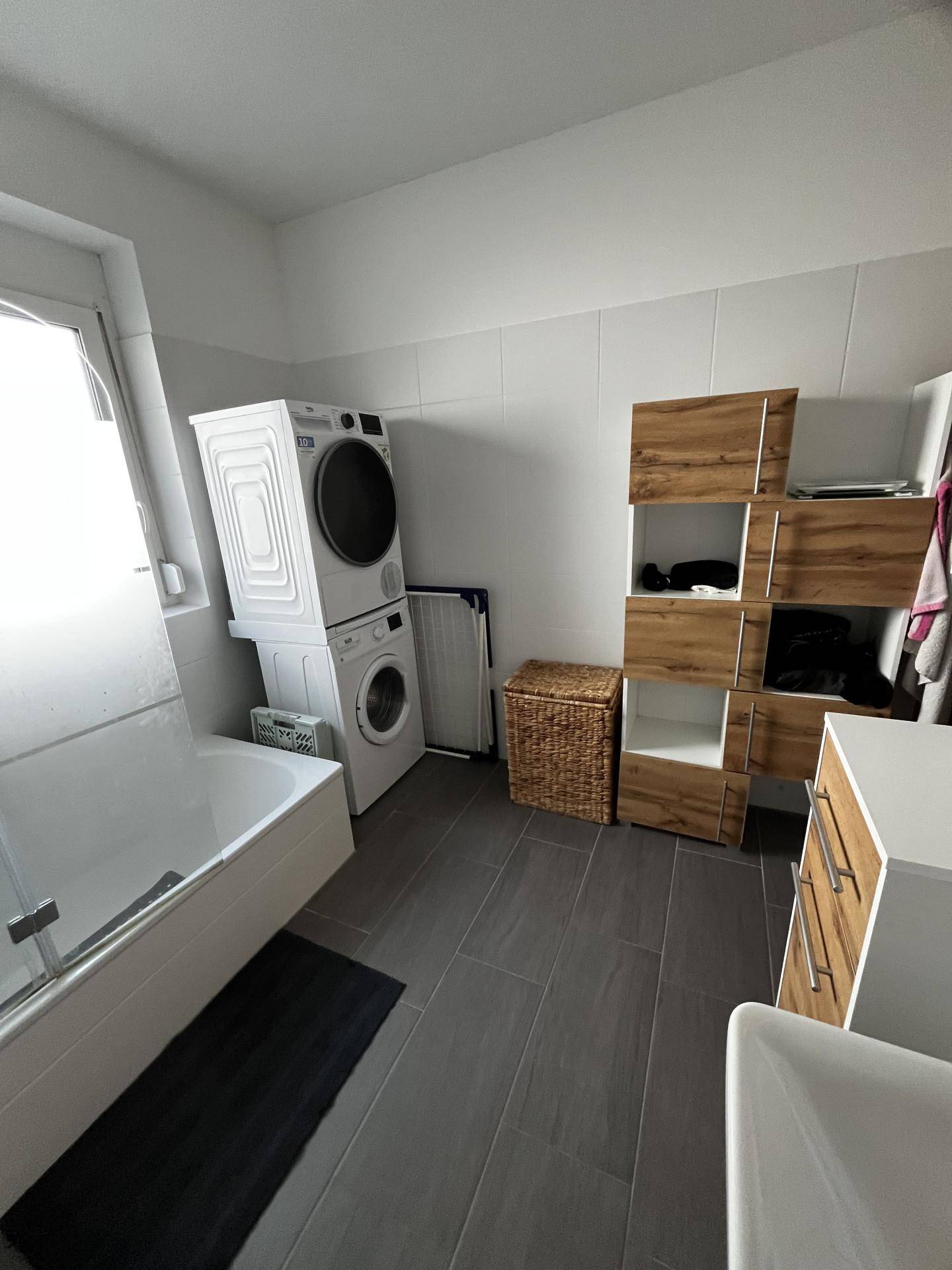 Badezimmer mit Badewanne, Waschmaschine, Trockner und modernen Holzregalen.