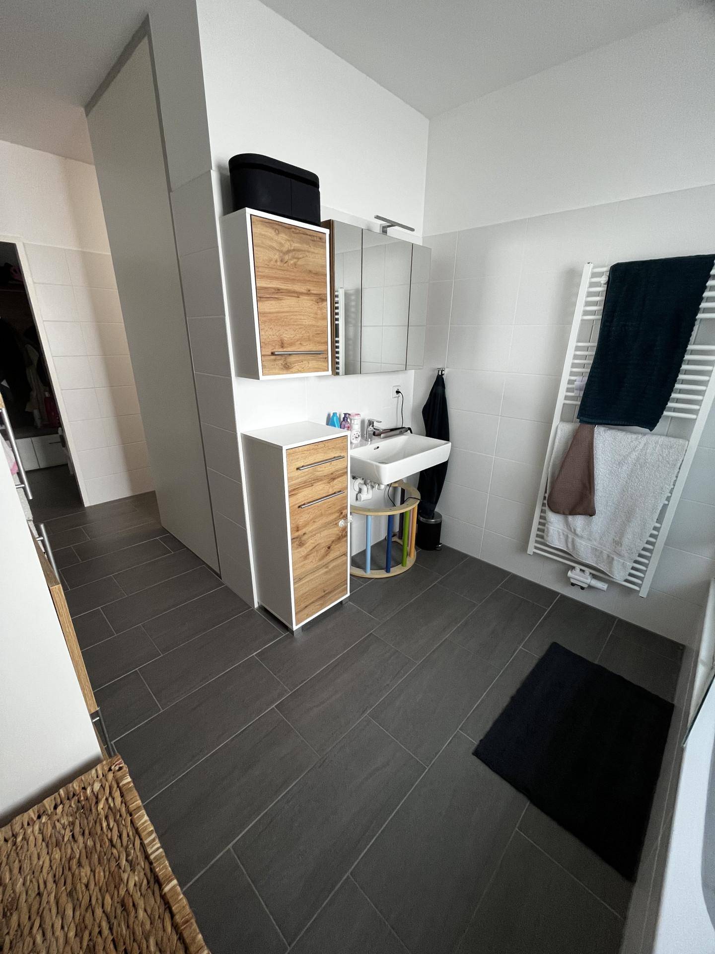 Modernes Badezimmer mit Waschbecken, Spiegelschrank, Handtuchheizkörper und Fliesenboden.