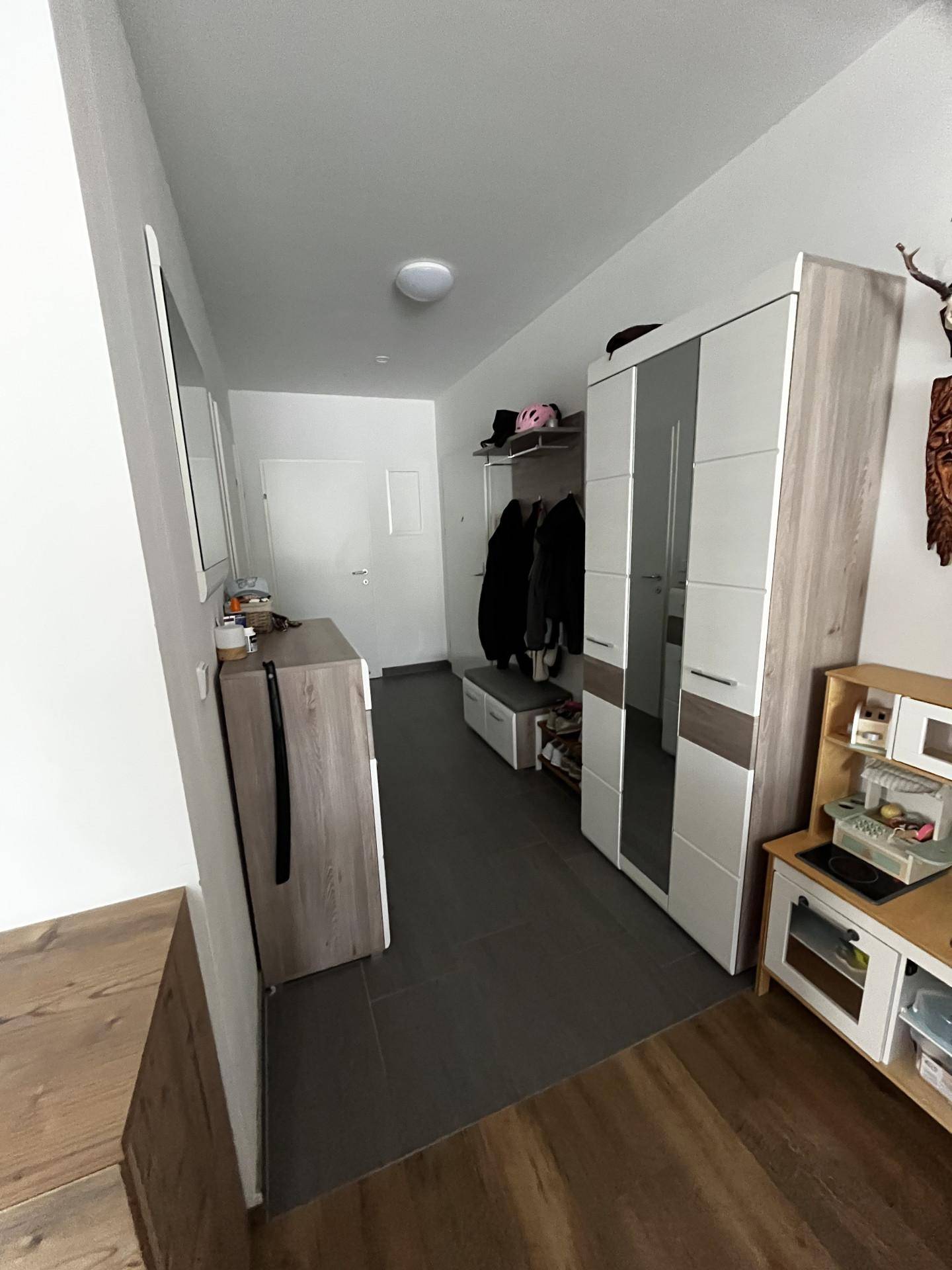 Eingangsbereich mit Garderobe, Spiegel und Holzboden, der zu den Wohnräumen führt.