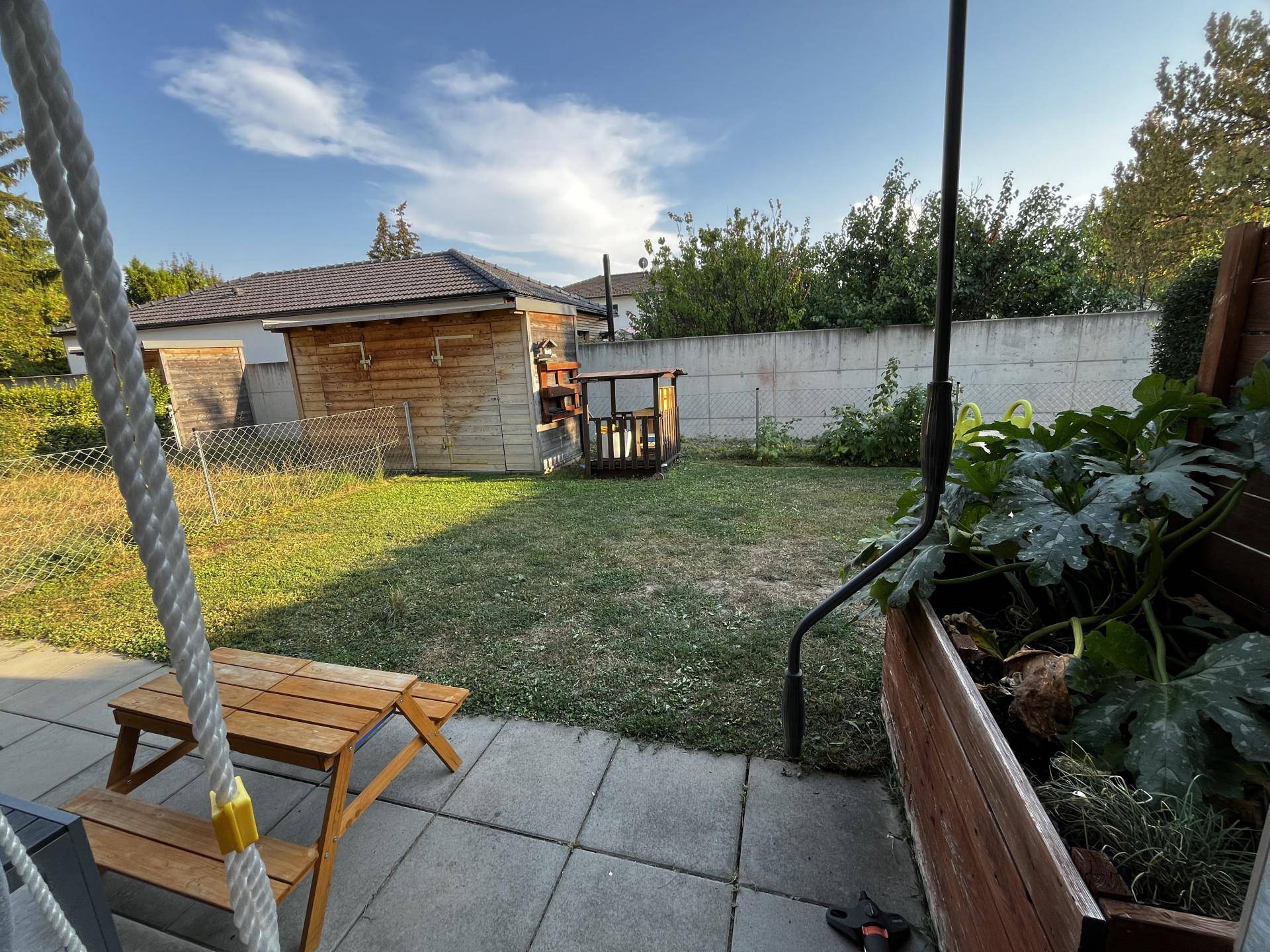 Hinterer Gartenbereich mit Rasen, Hochbeet und einem kleinen Holzschuppen im Hintergrund.