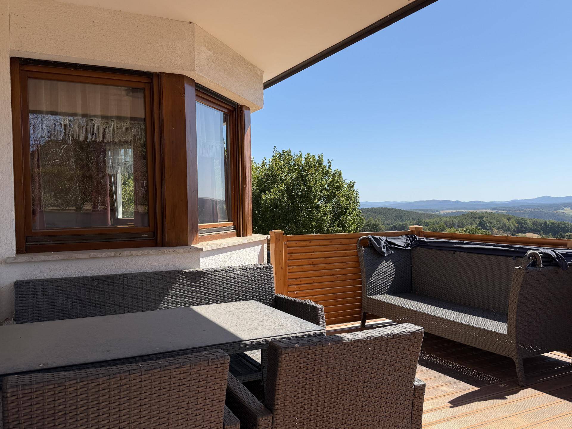 Möblierte Terrasse mit Rattanmöbeln und weitem Blick in die grüne, hügelige Landschaft.