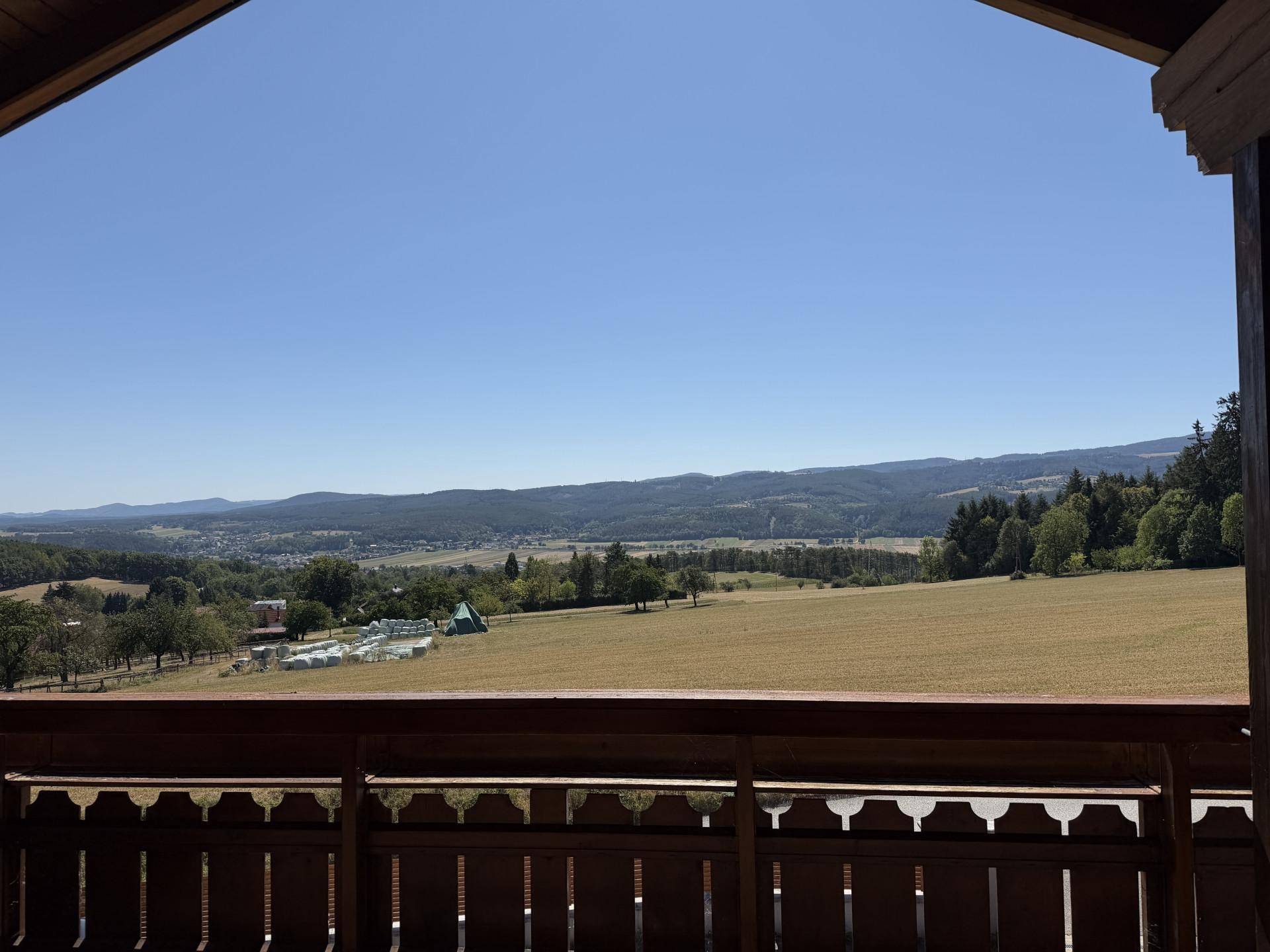 Panoramablick von einem Balkon über weite Felder und eine malerische, hügelige Landschaft.