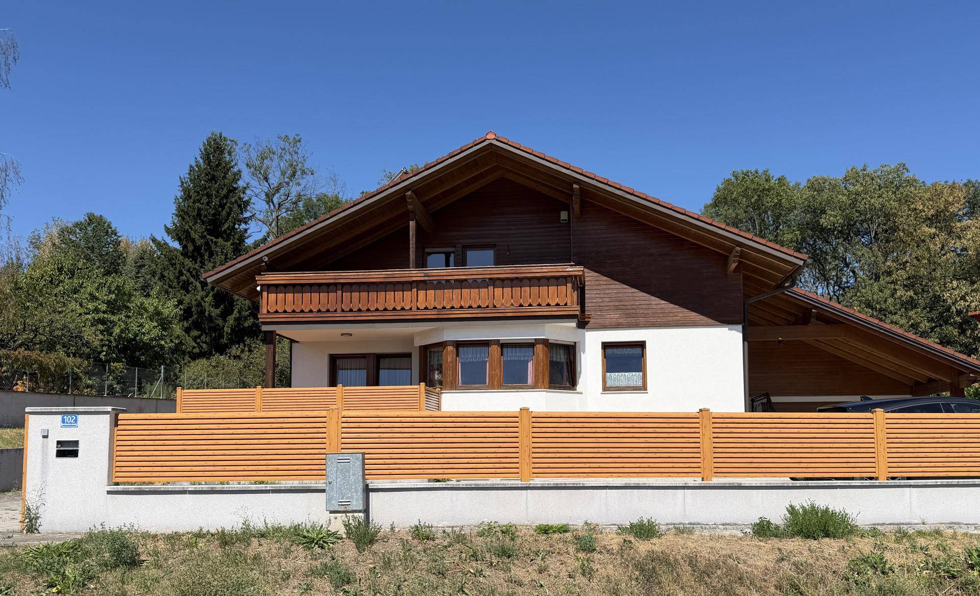 Vorderansicht des Hauses mit Holzzaun, Satteldach und einem Balkon im Obergeschoss.