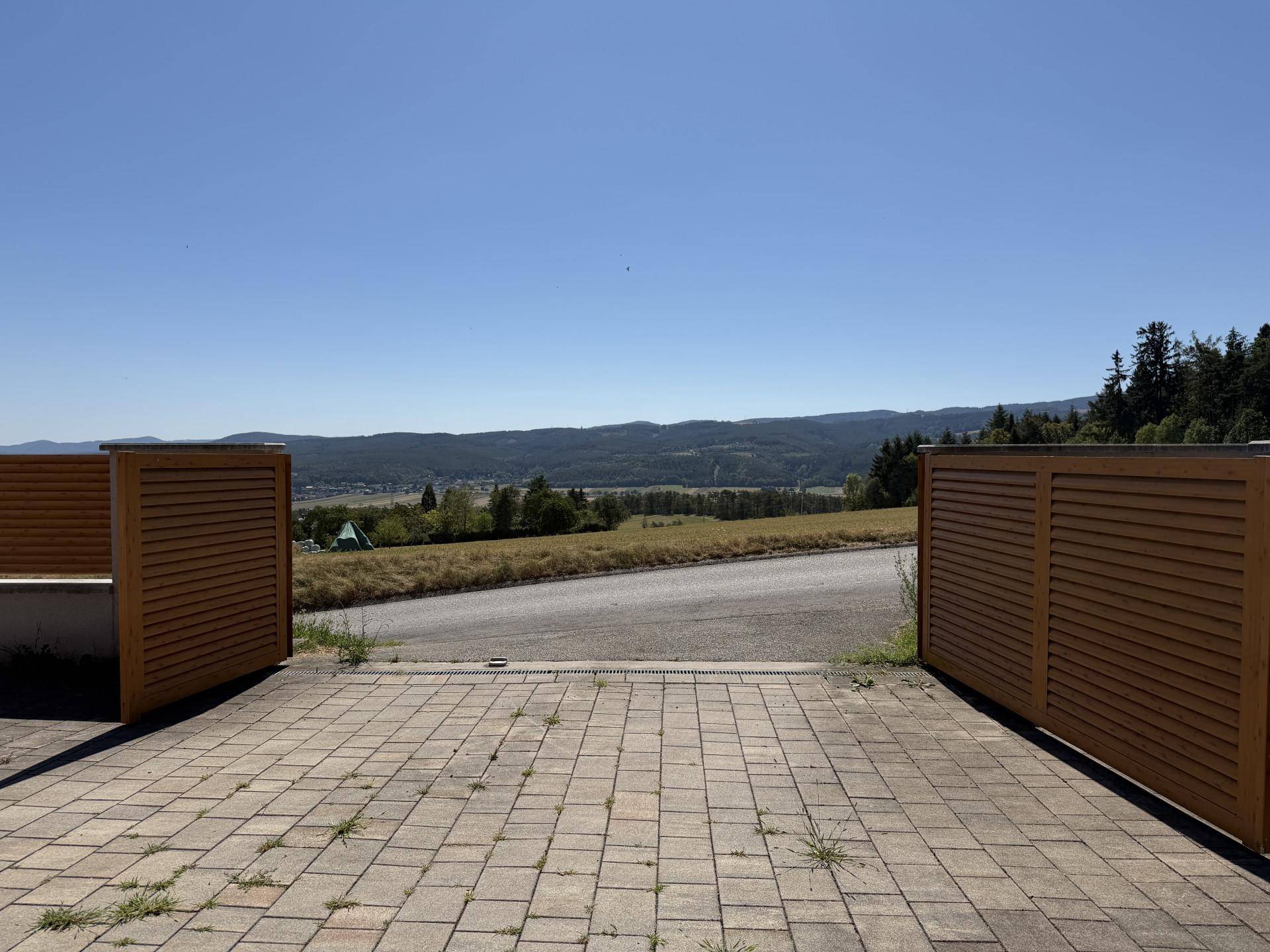 Gepflasterter Vorplatz mit Holztoren und weitem Blick über die umliegende Landschaft.