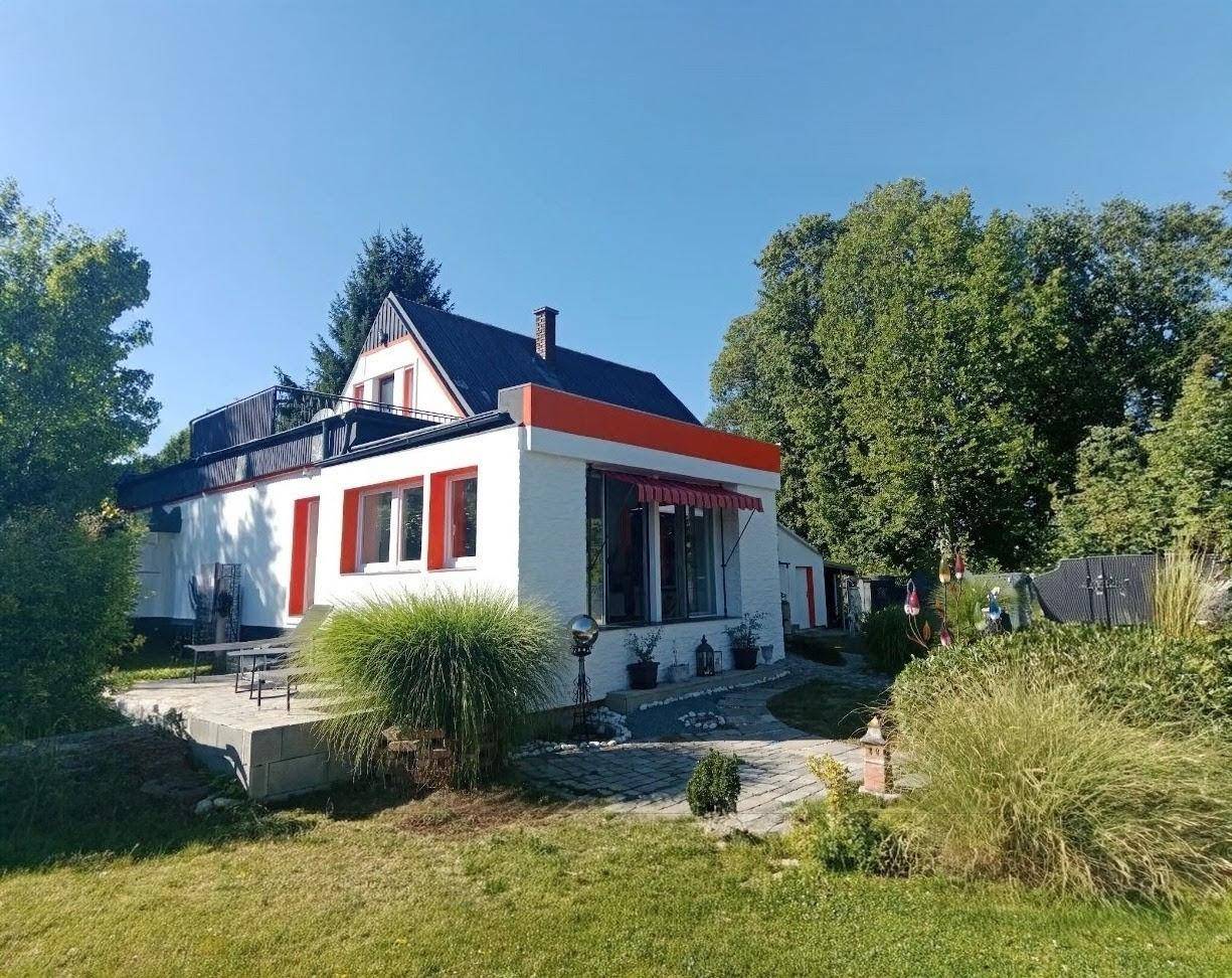 Seitenansicht des Hauses mit Terrasse, Gartenbereich und großen Fenstern an einem sonnigen Tag.