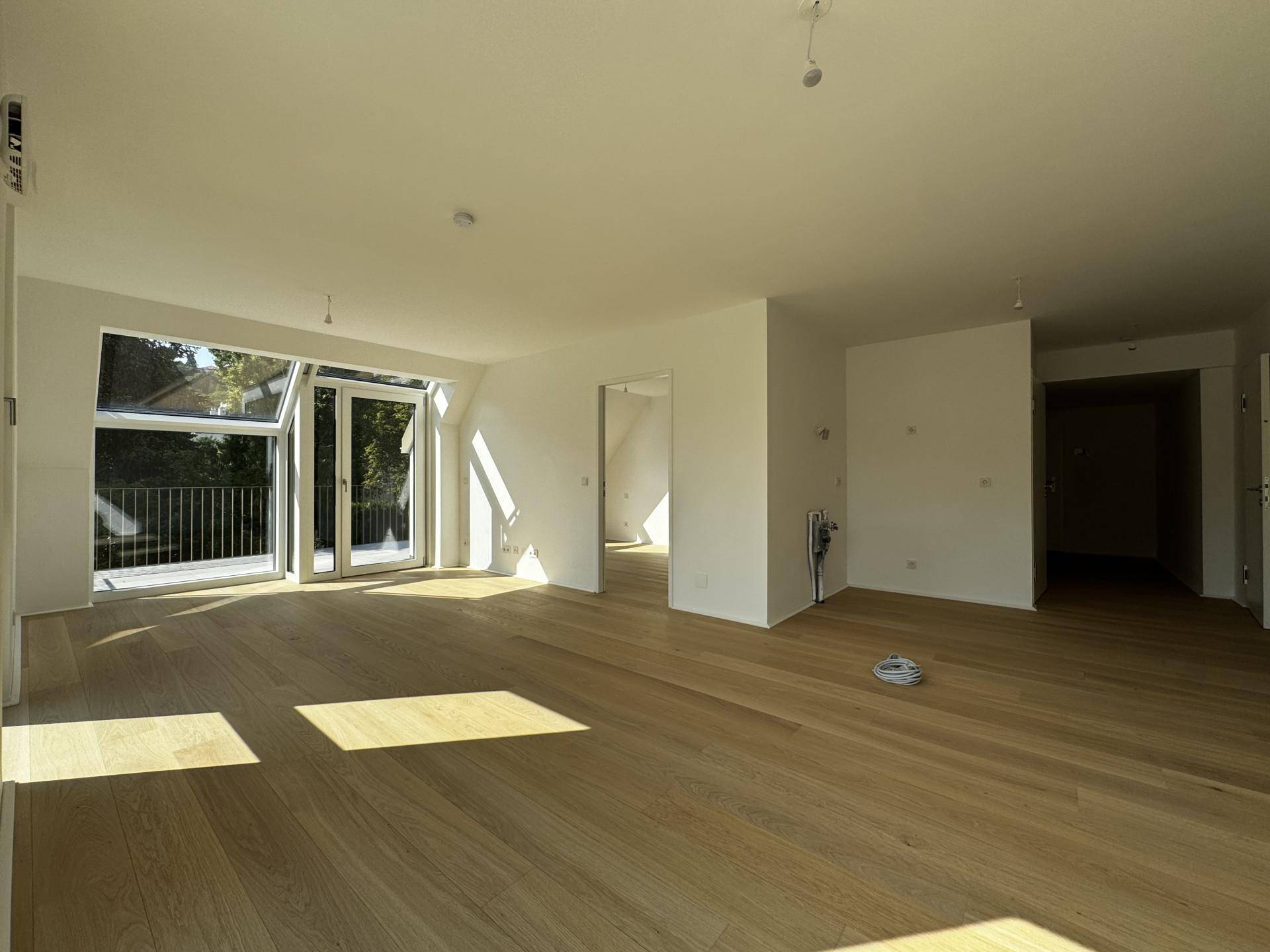 Geräumiger, heller Wohnbereich mit Holzboden und großen Fensterfronten, die viel Licht hereinlassen.