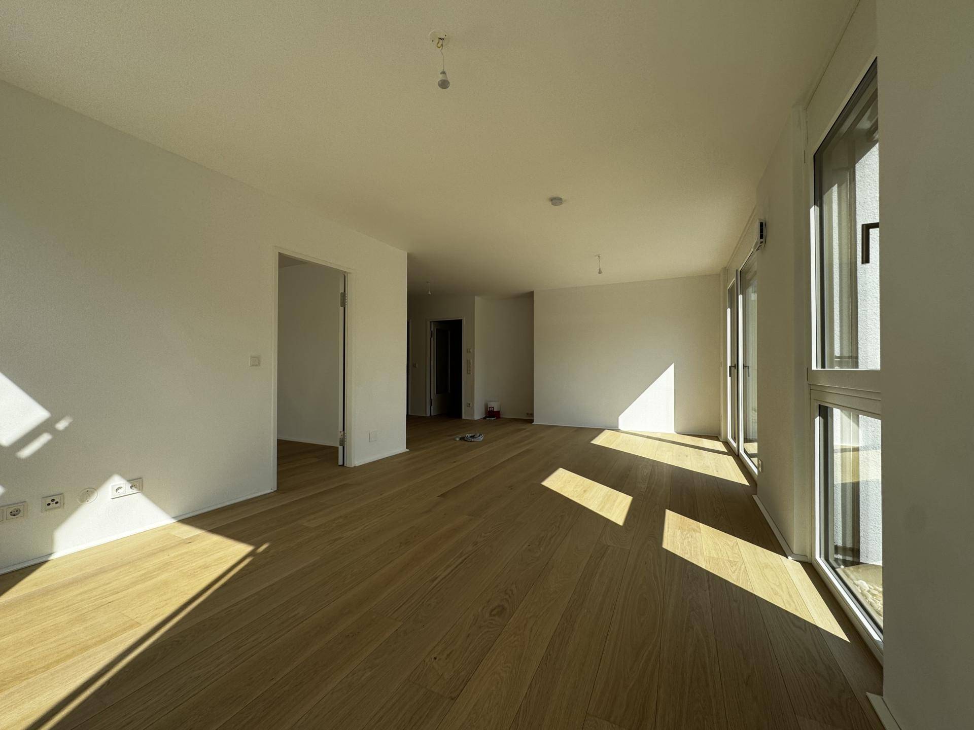 Moderner, leerer Wohnraum mit Eichenparkett und großen Fenstern, die viel Sonnenlicht bieten.