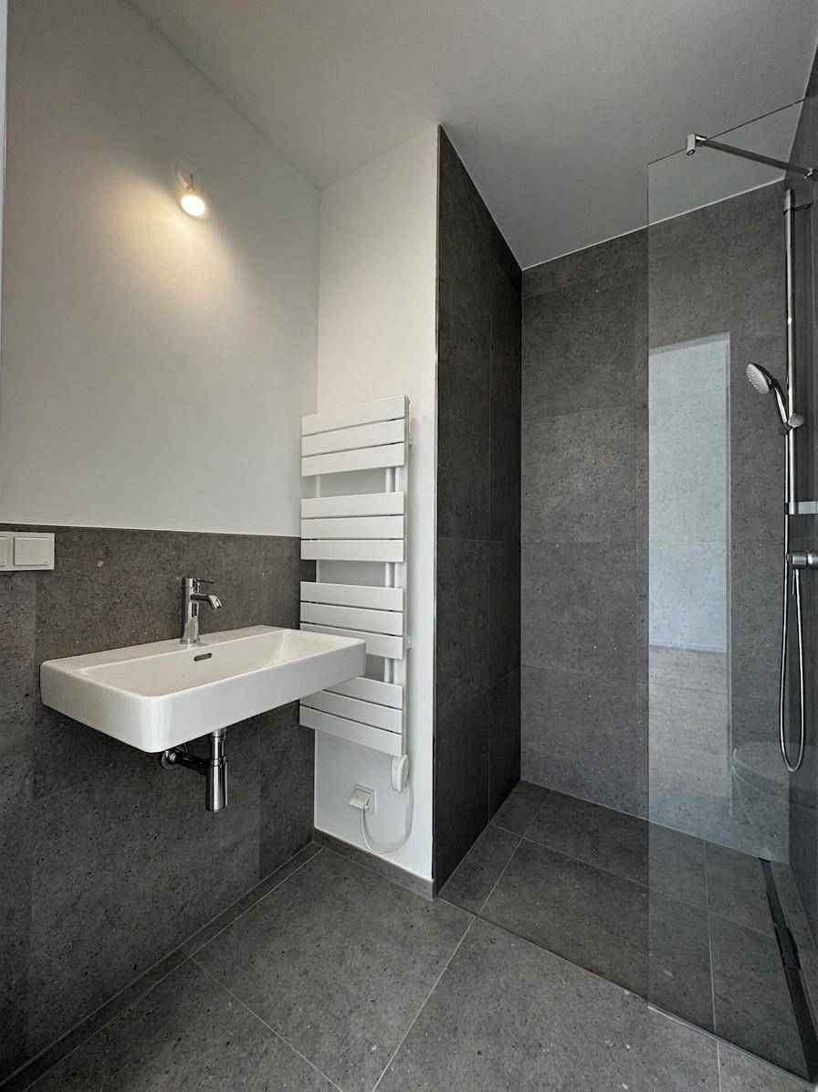 Modernes Badezimmer mit grauen Fliesen, Waschtisch, bodengleicher Dusche und Handtuchheizkörper.