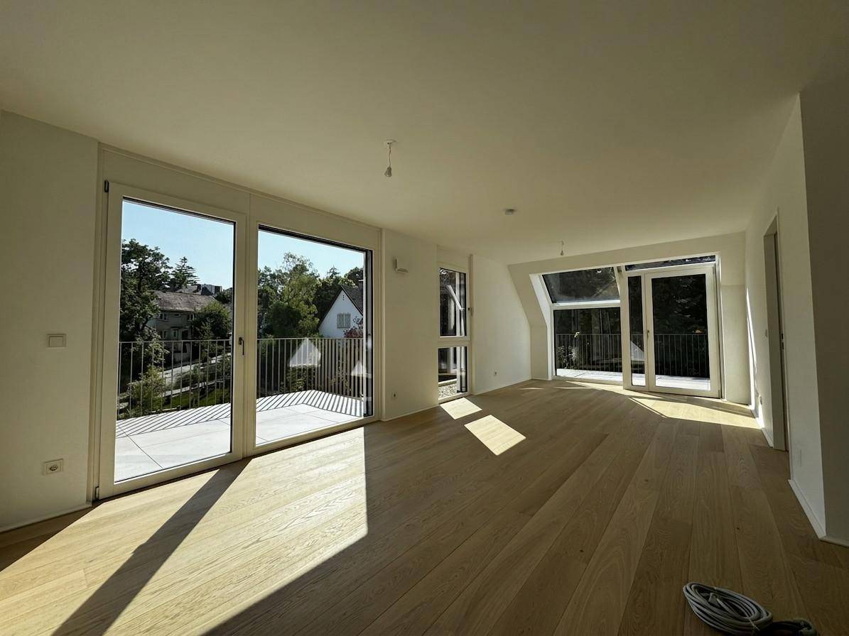 Helles, leeres Wohnzimmer mit Eichenparkett und großen Fenstern mit Zugang zur Terrasse.