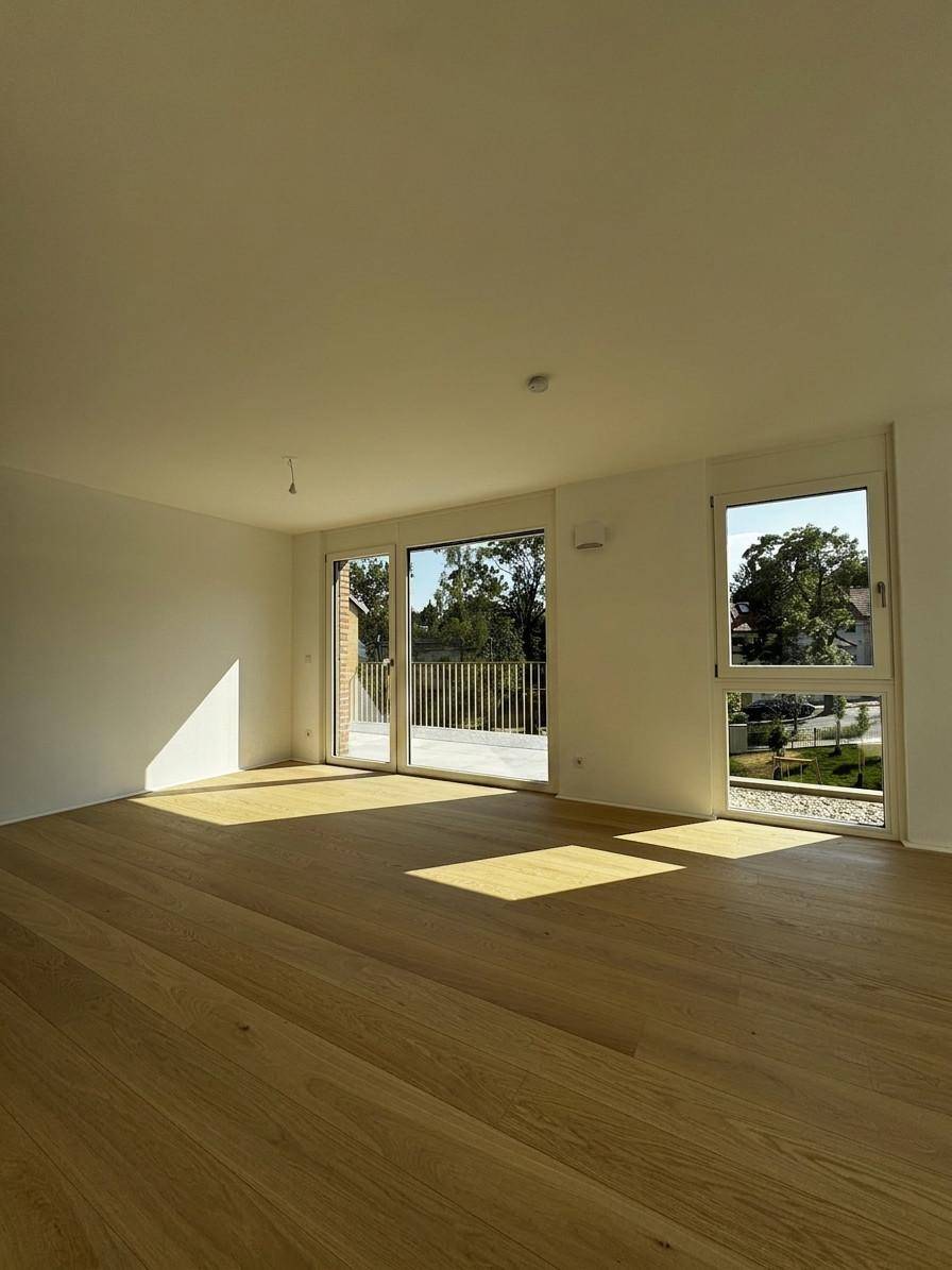 Lichtdurchflutetes Wohnzimmer mit hellem Parkettboden und weitem Blick ins Grüne.