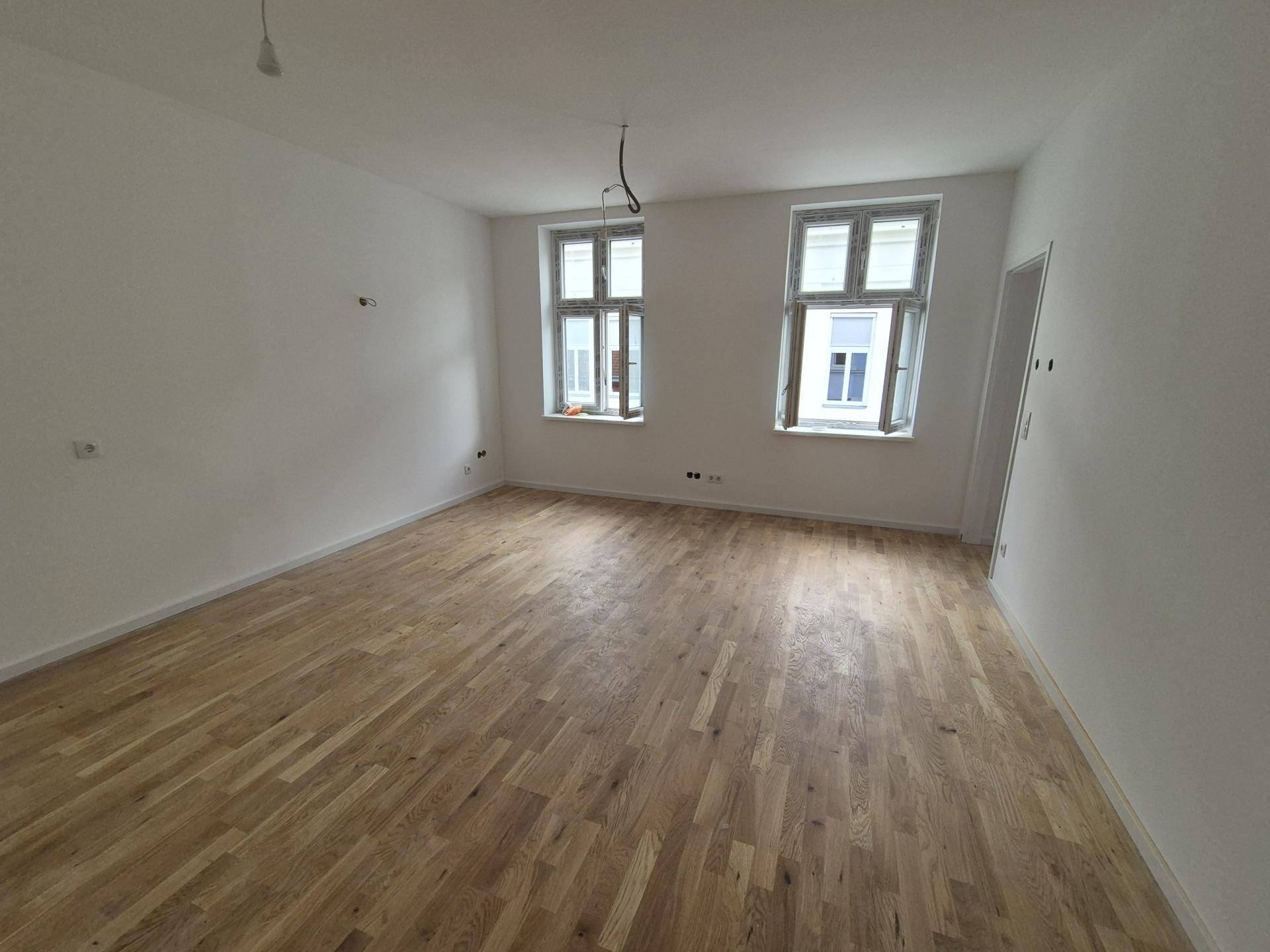 Heller, leerer Raum mit neuem Parkettboden und zwei großen Fenstern, bereit zum Einzug.