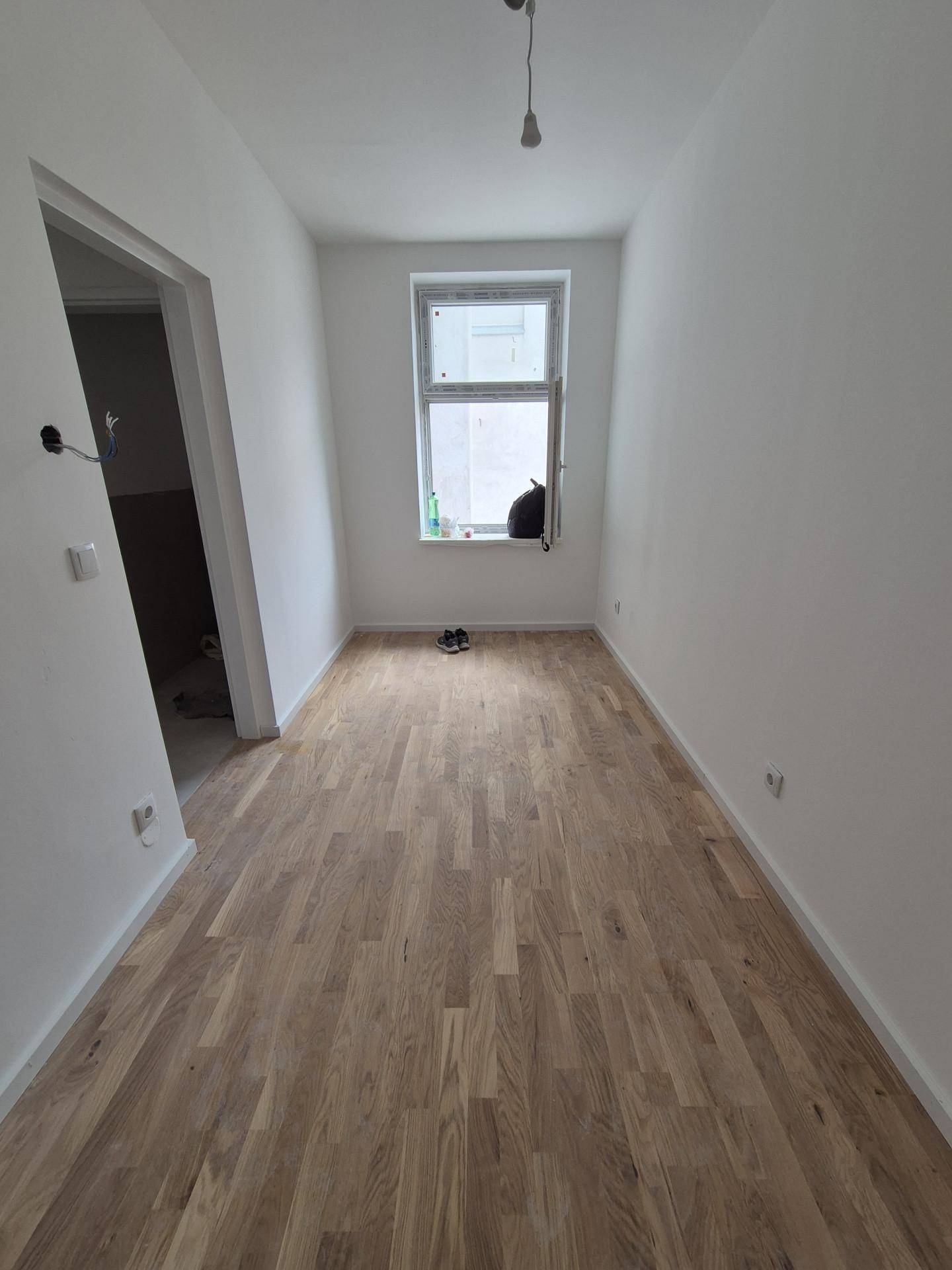Schmaler, heller Raum mit neuem Parkettboden und einem Fenster, ideal als Schlaf- oder Arbeitszimmer.