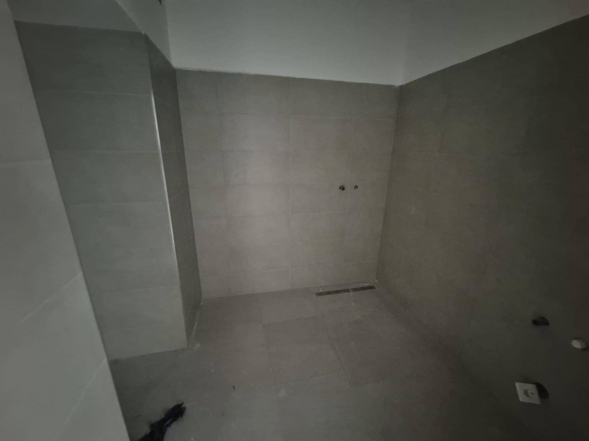 Unfertiges Badezimmer mit grauen Fliesen an Wänden und Boden, bereit für die Installation der Sanitärobjekte.