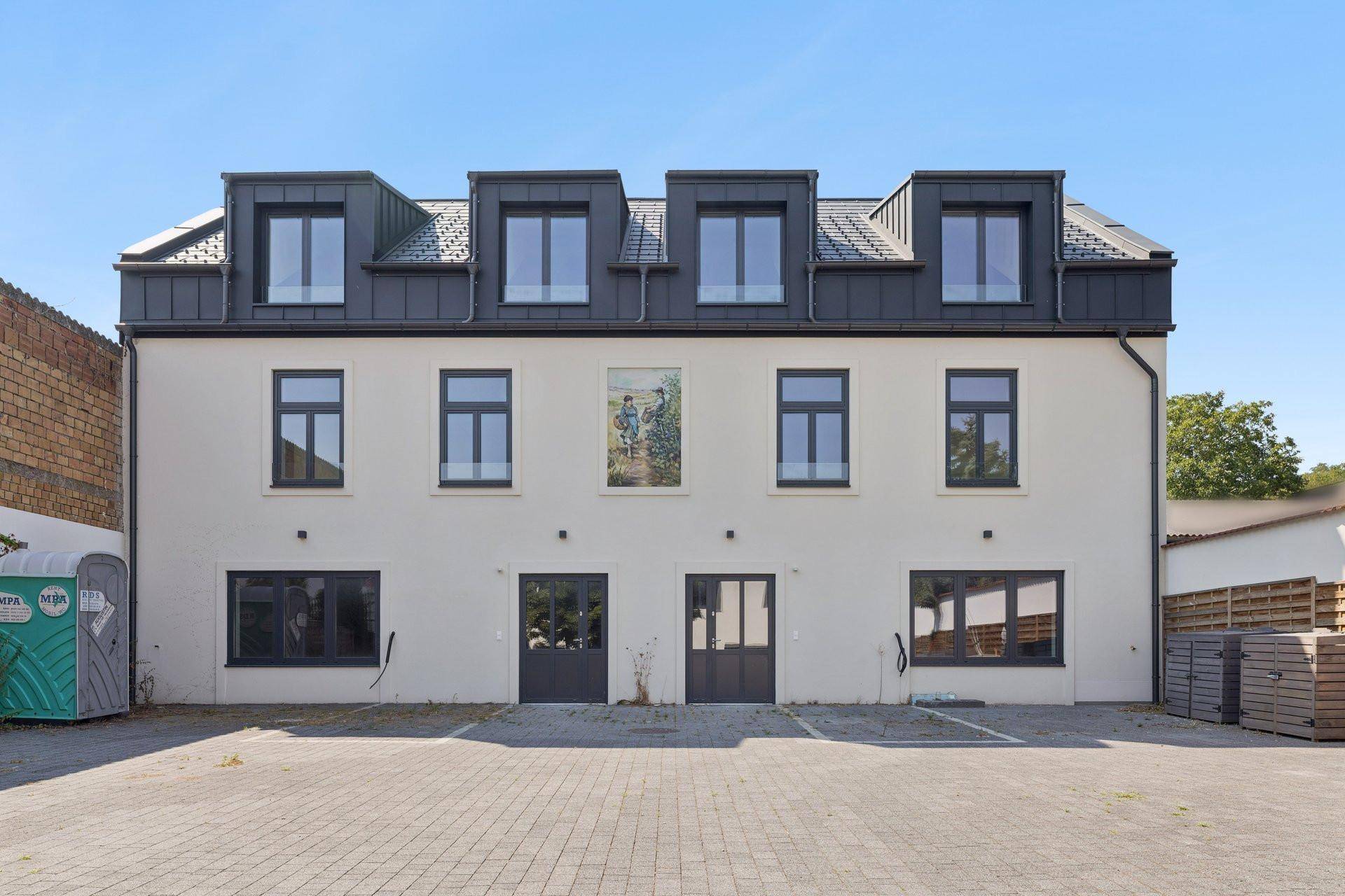 Frontansicht des Neubaus mit gepflastertem Parkplatz und mehreren Fenstern im Obergeschoss.