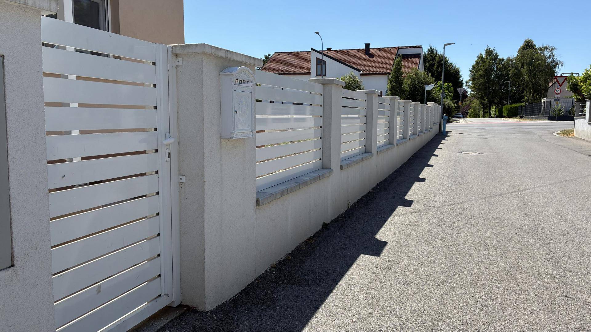 Moderne weiße Zaunanlage mit Tor entlang der Straße.