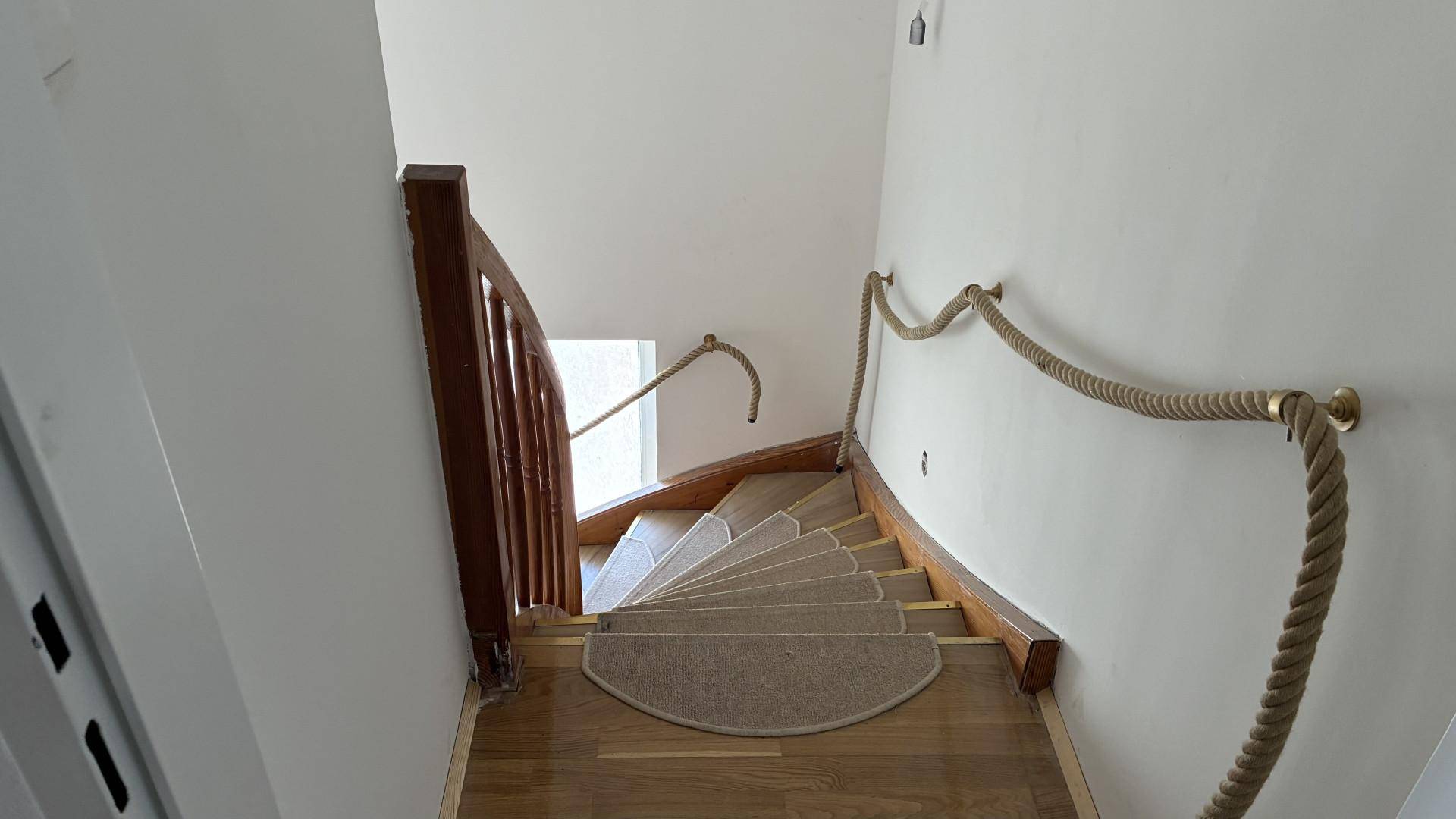 Wendeltreppe mit Holzstufen, Teppichläufer und einem dekorativen Seilgeländer.
