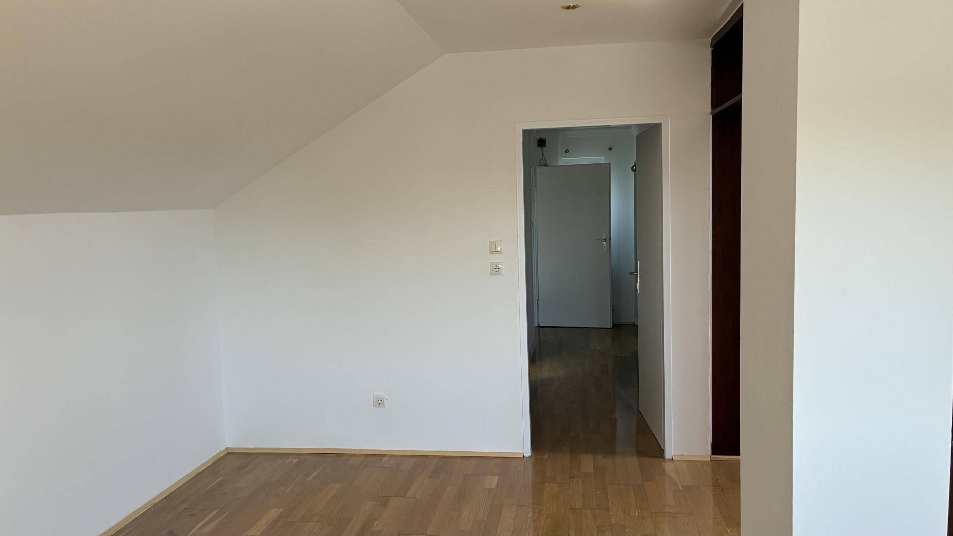 Leeres Dachzimmer mit schrägen Wänden und hellem Holzfußboden.