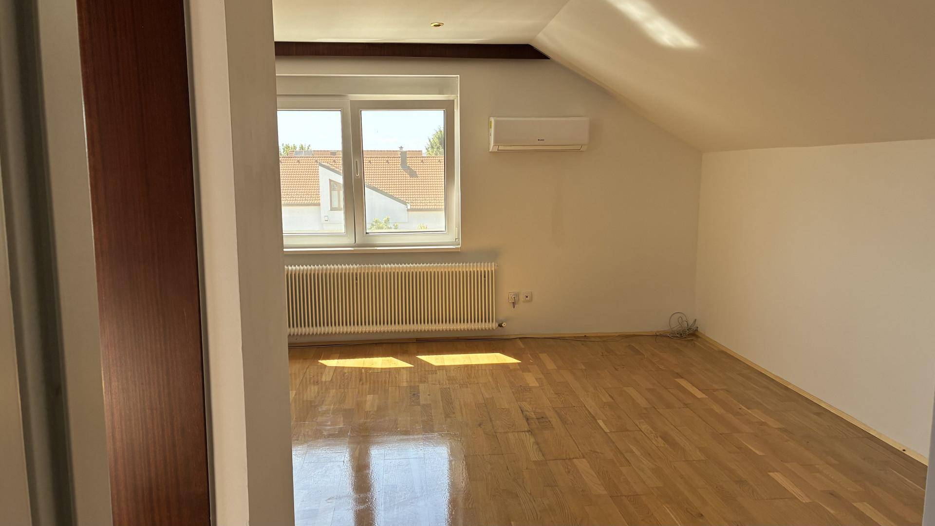 Helles Dachzimmer mit schrägen Wänden, Holzfußboden und Klimaanlage.