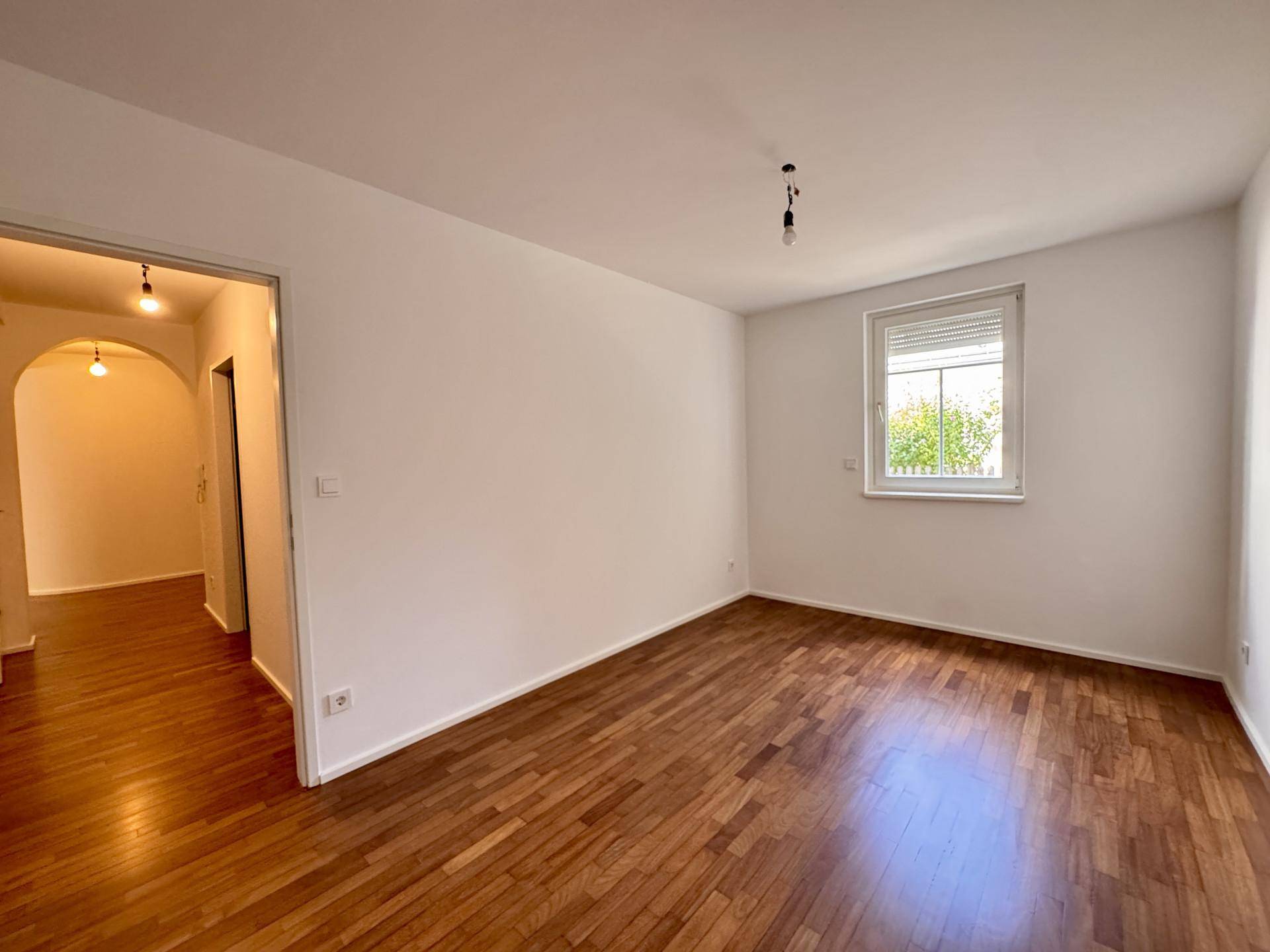 Geräumiges Zimmer mit Parkettboden und Zugang zu einem Flur durch einen eleganten Bogen.