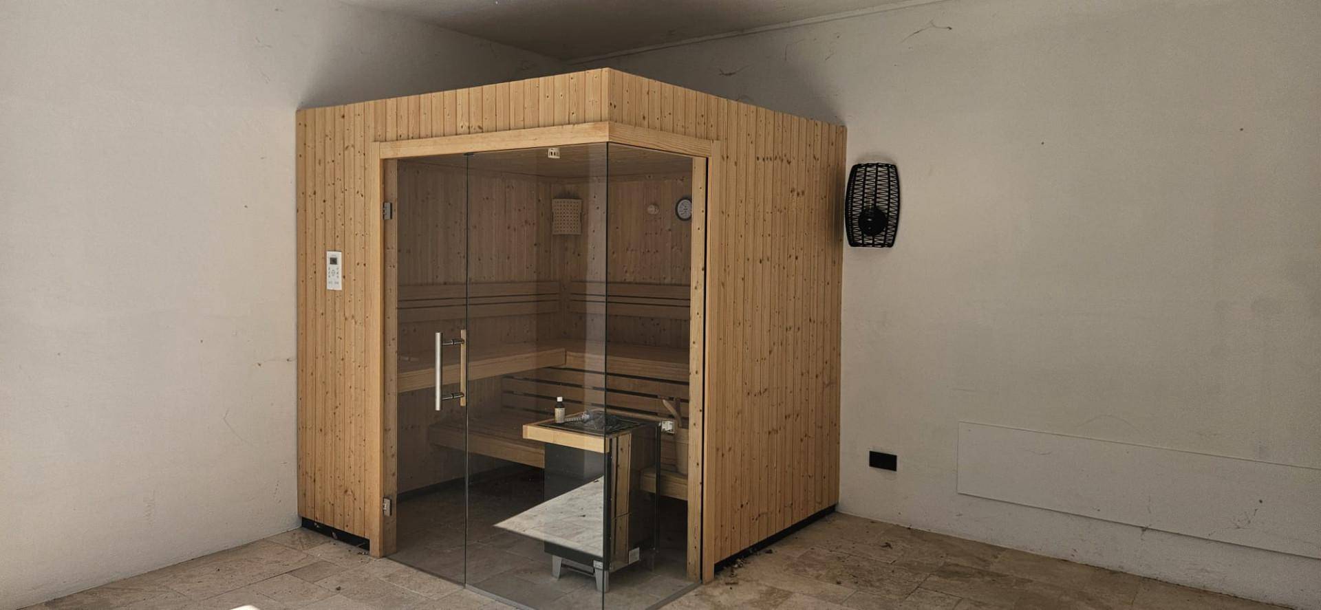 Moderne Holzsaunakabine mit Glastür in einem schlichten Raum, bereit zur Nutzung.