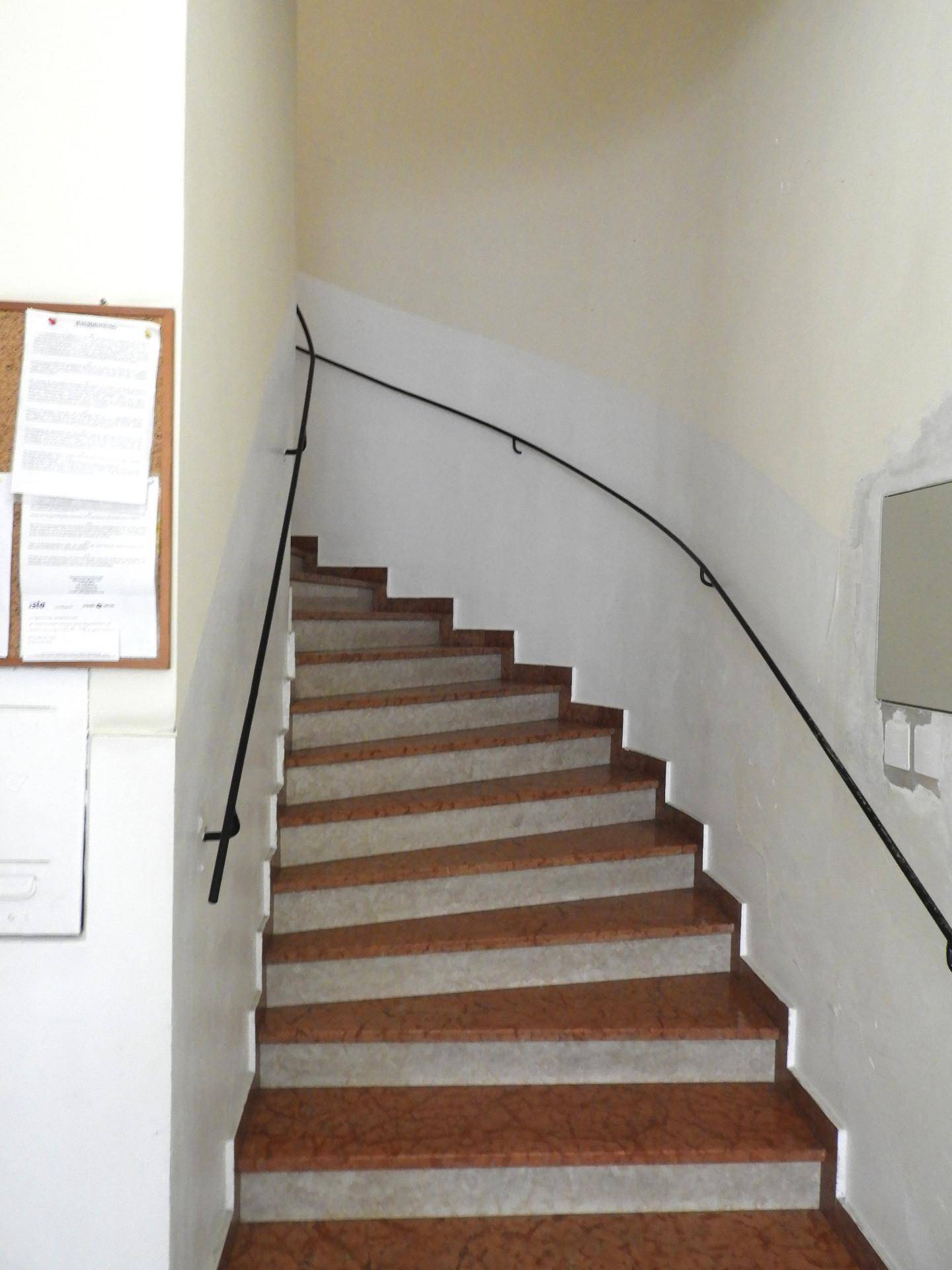 Treppenhaus mit Marmorstufen und einem schlichten schwarzen Handlauf in einem Altbau.