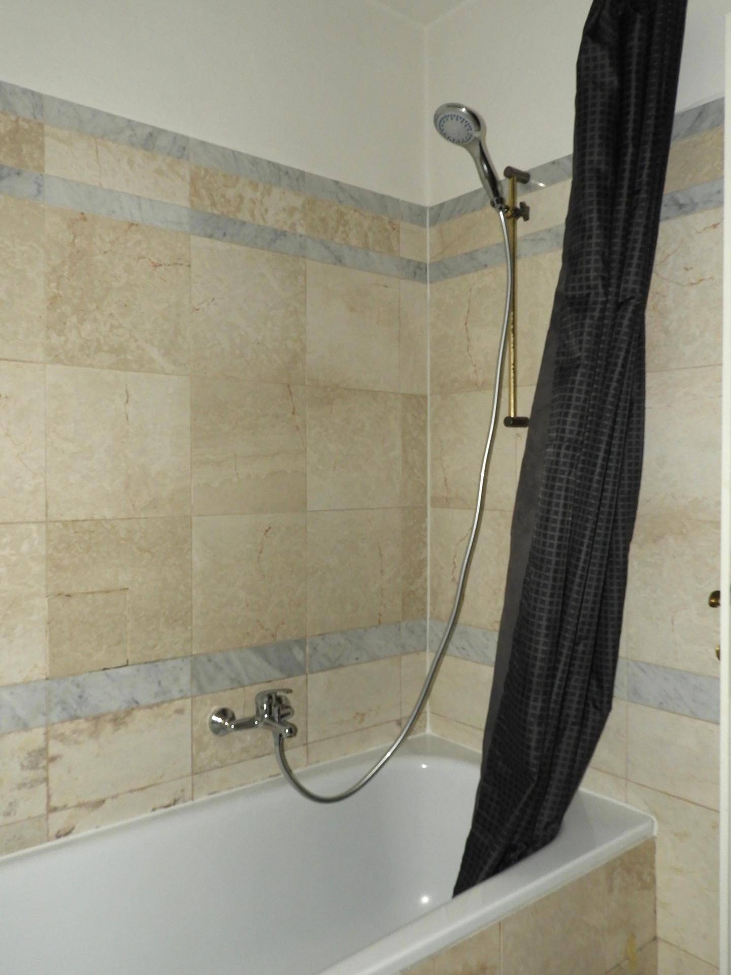Badezimmer mit Badewanne und Duschvorhang, gefliest mit hellen Marmorfliesen.