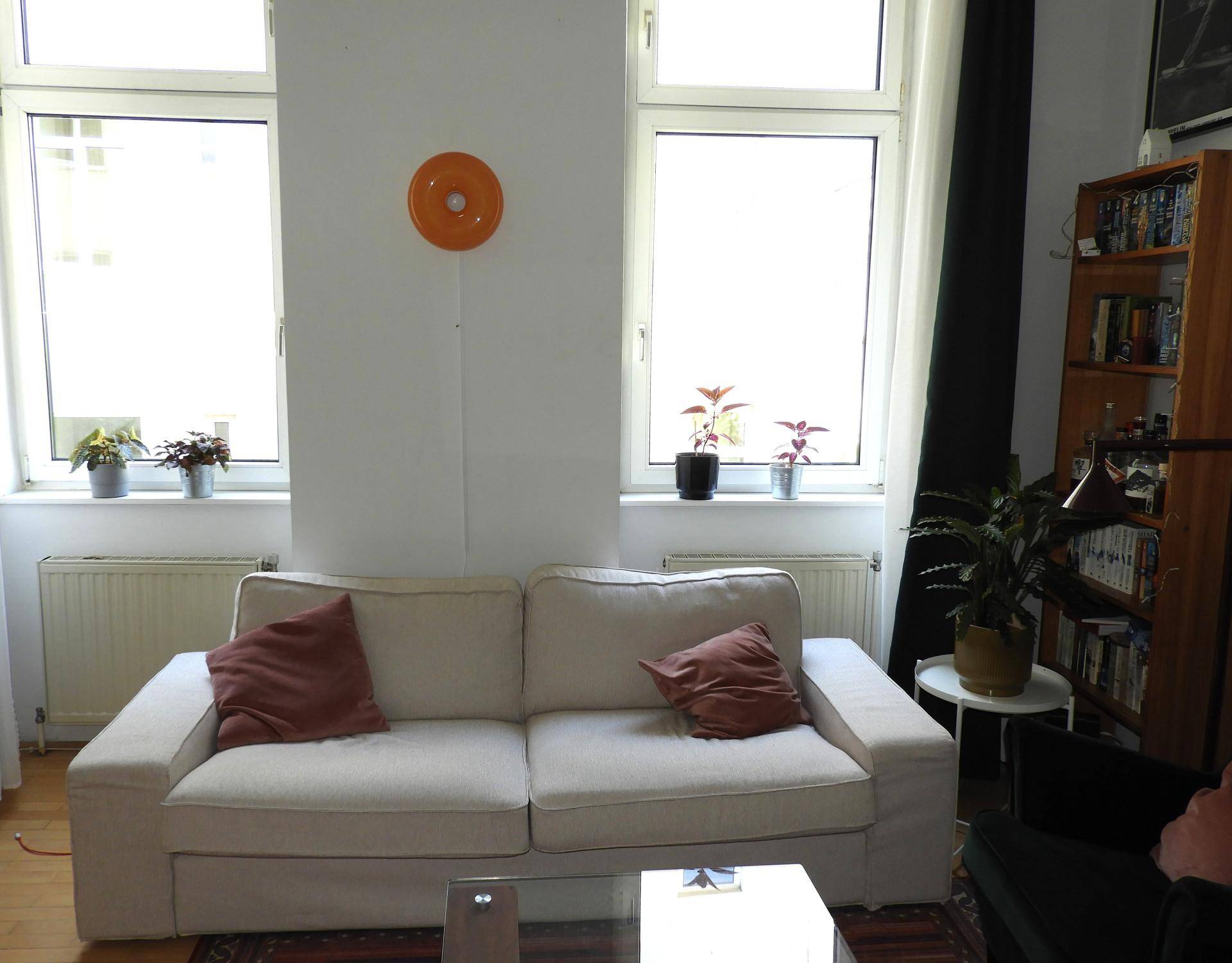 Helles Wohnzimmer mit beigem Sofa, Holzboden und großen Fenstern.