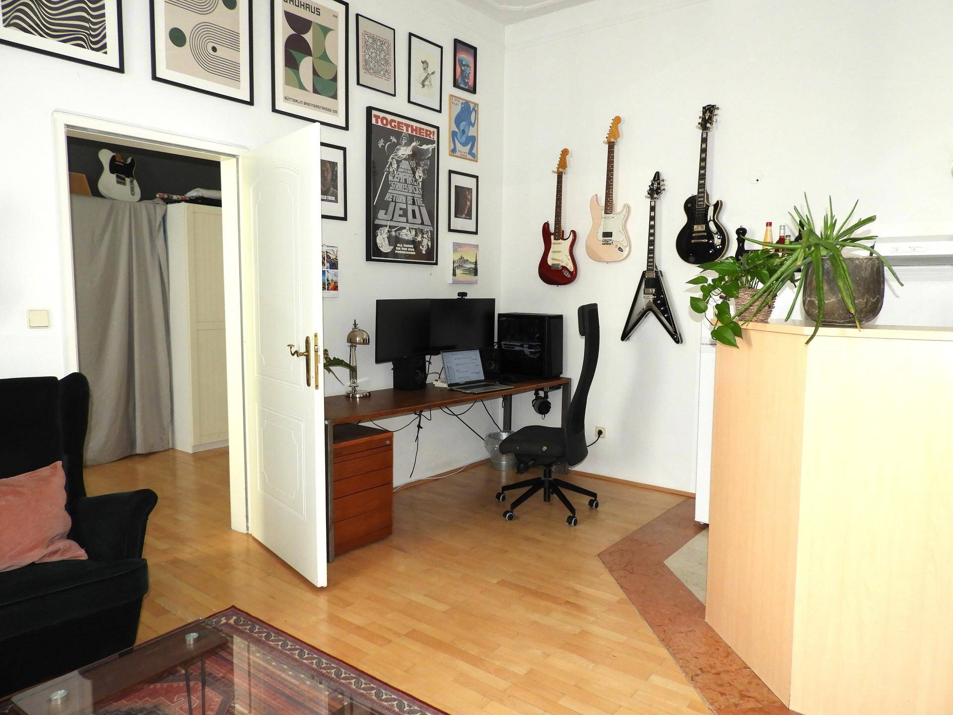 Kreativer Arbeitsbereich mit Holzboden, vielen Bildern und Musikinstrumenten an der Wand.