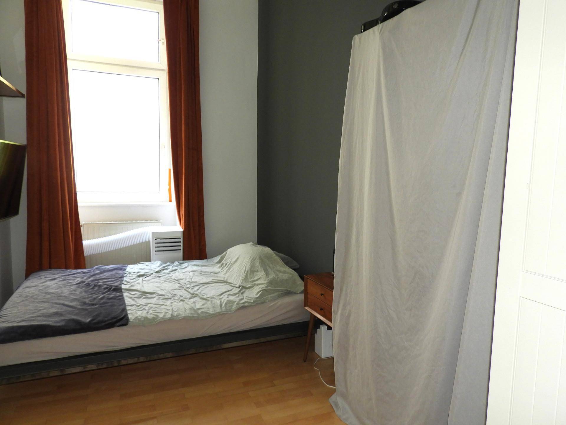 Schlafzimmer mit Holzboden, Einzelbett und einem großen Fenster für natürliche Belichtung.
