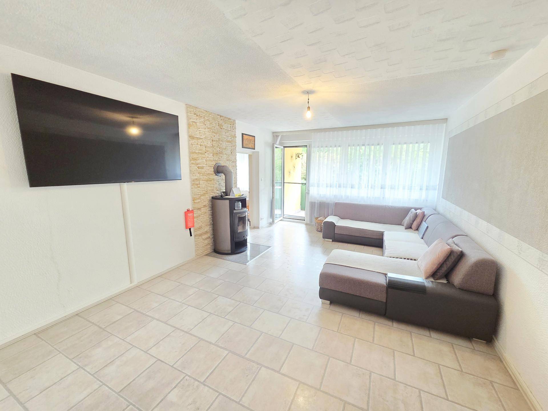 Geräumiges Wohnzimmer mit modernem Kaminofen, Fliesenboden und Zugang zum Balkon.