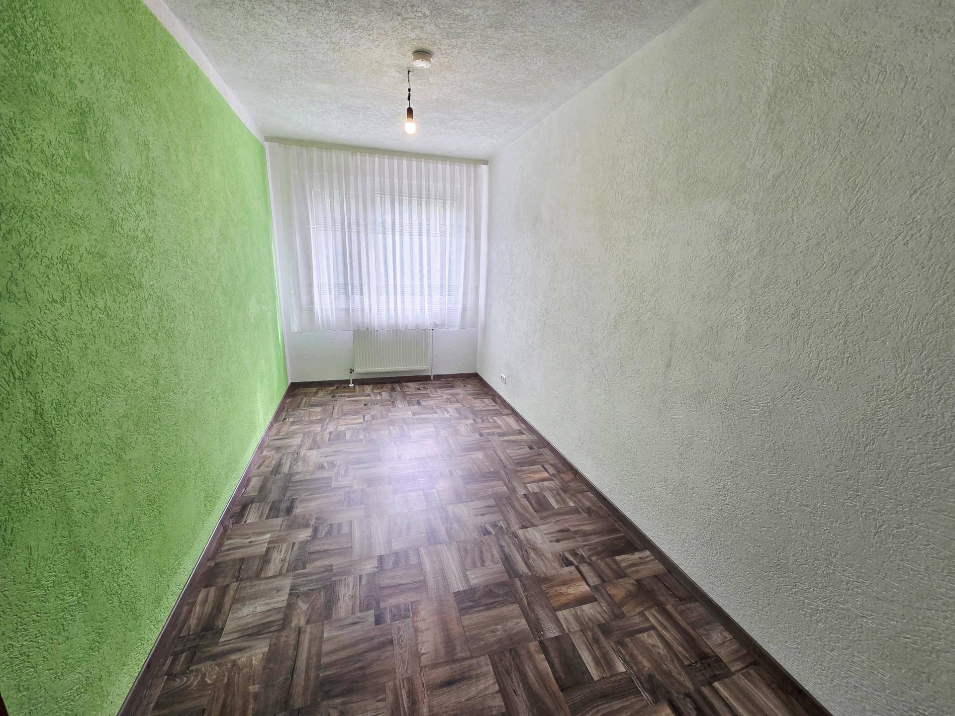 Leeres Zimmer mit auffälliger grüner Akzentwand und Parkettboden.