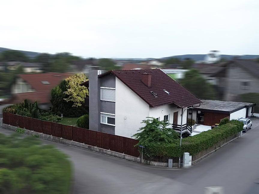 Vogelperspektive eines Einfamilienhauses mit Garten, Zaun und einem Auto auf dem Stellplatz.