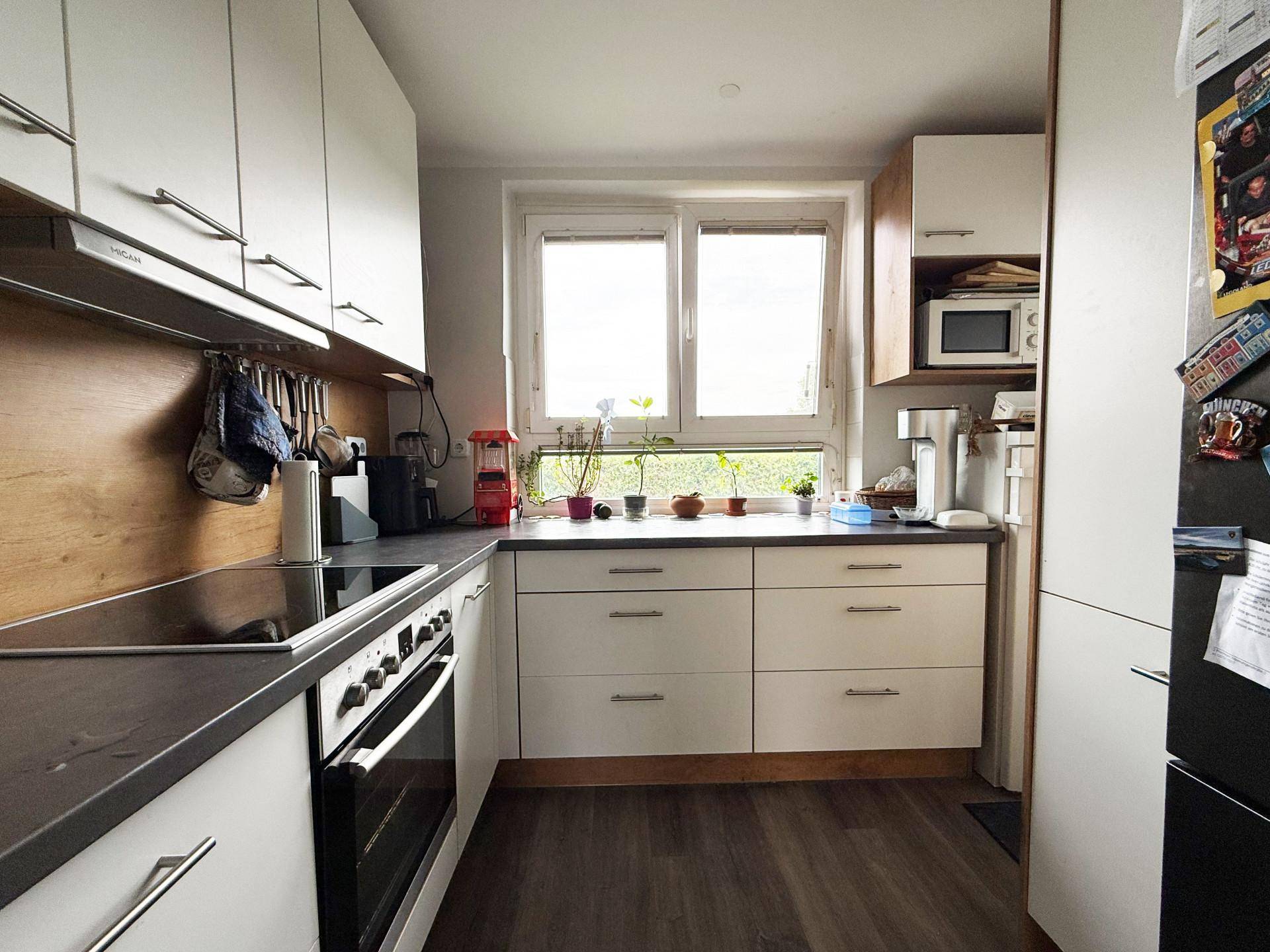 Helle Küche mit weißen Schränken, Holzrückwand und Blick nach draußen durch das Fenster.