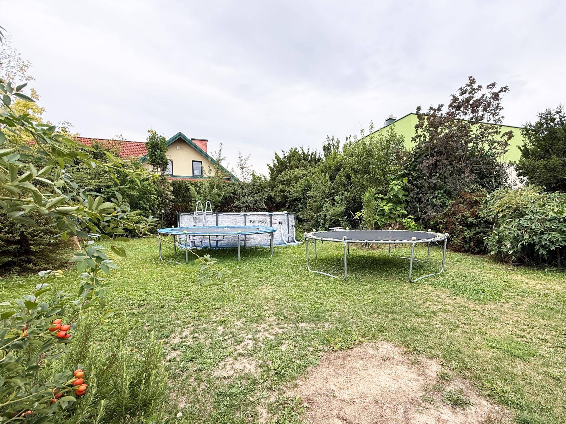 Großer Garten mit Rasenfläche, Pool, Trampolin und üppiger Bepflanzung.