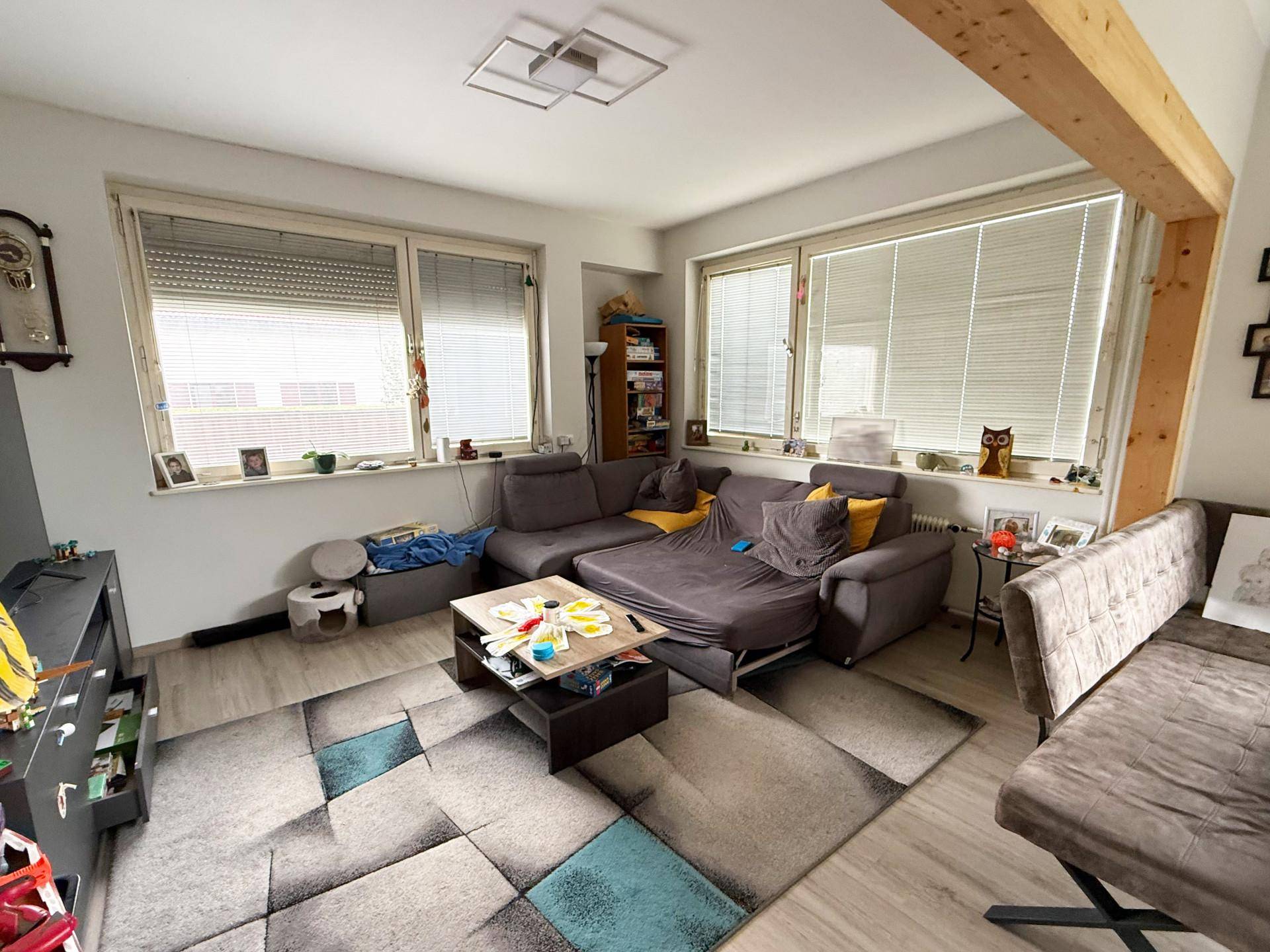 Gemütliches Wohnzimmer mit großem Ecksofa, Teppich und viel Tageslicht durch die Fenster.