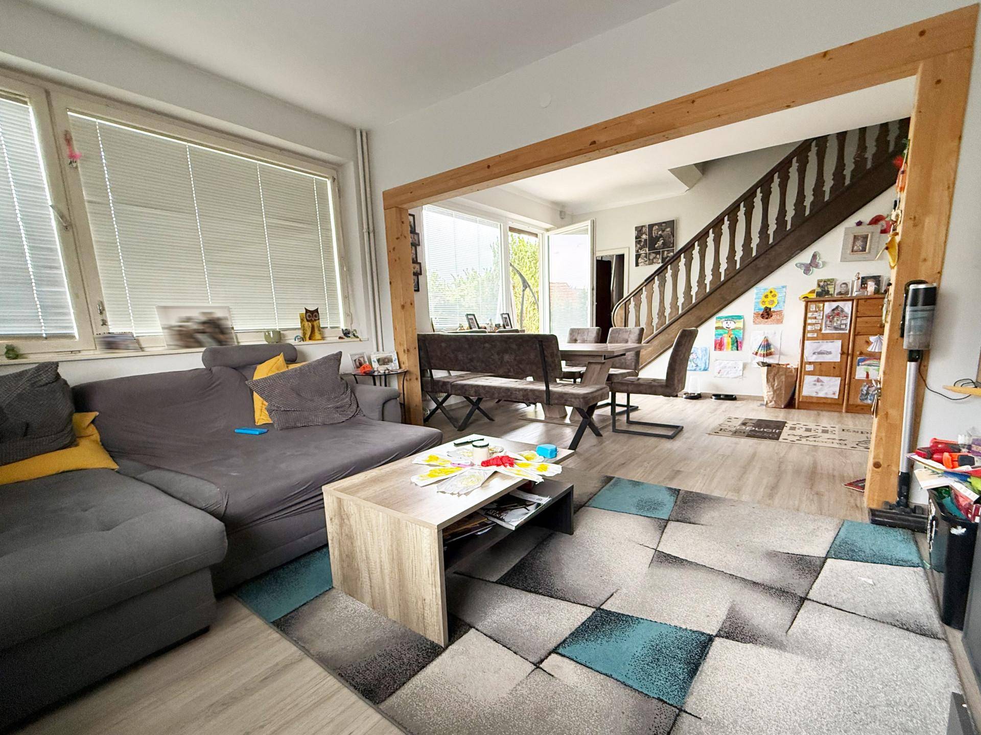 Heller Wohnbereich mit Sofa, Esstisch und Treppe, die in den oberen Stock führt.