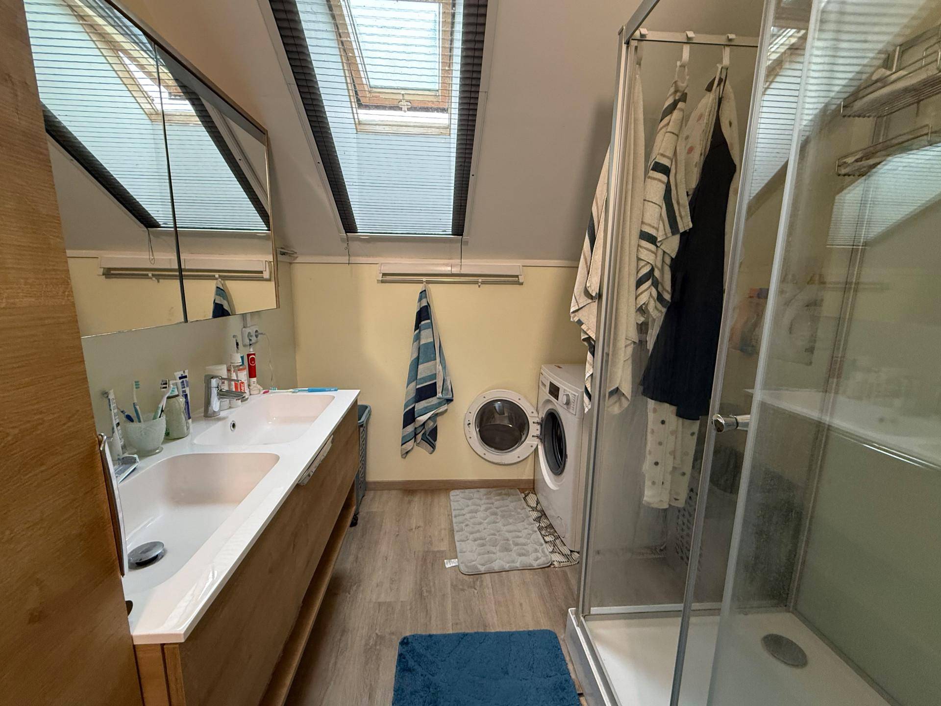 Dachgeschoss-Badezimmer mit Doppelwaschbecken, Waschmaschine, Duschkabine und Dachfenstern.