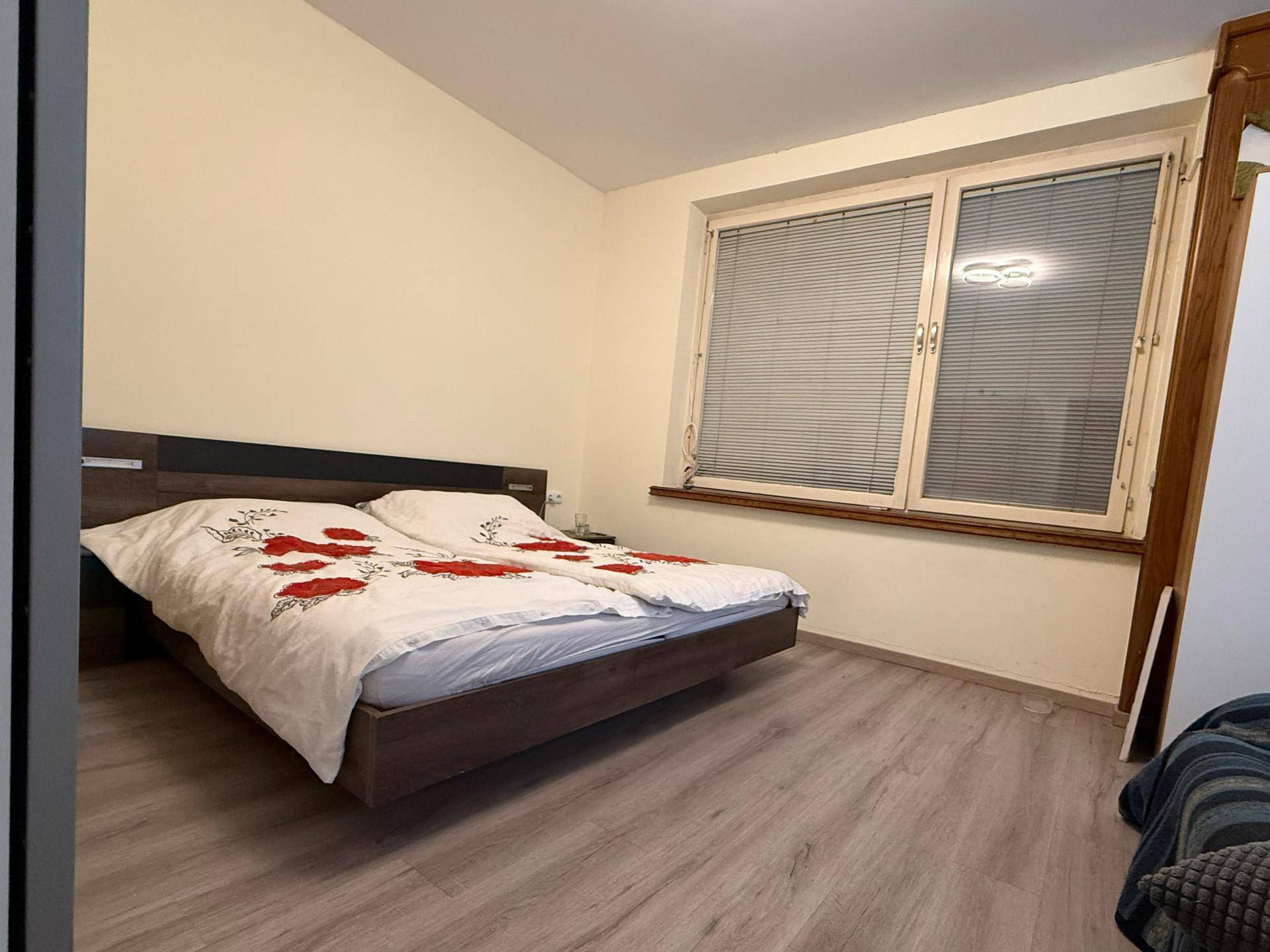 Schlafzimmer mit Doppelbett und großem Fenster, das viel Tageslicht hereinlässt.