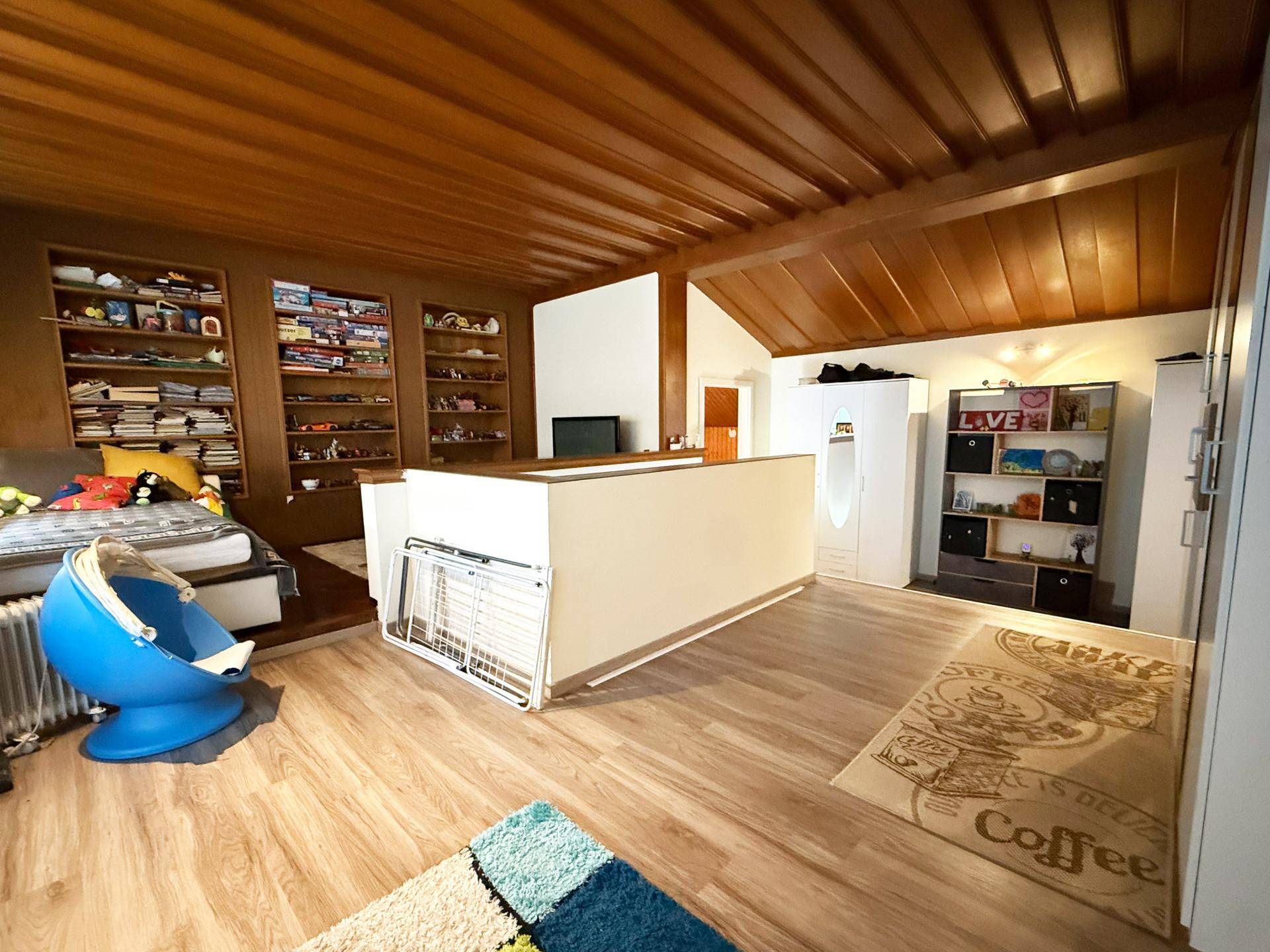 Gemütlicher Wohnbereich mit Holzdecke, Einbauregalen und Blick auf einen Schlafbereich.